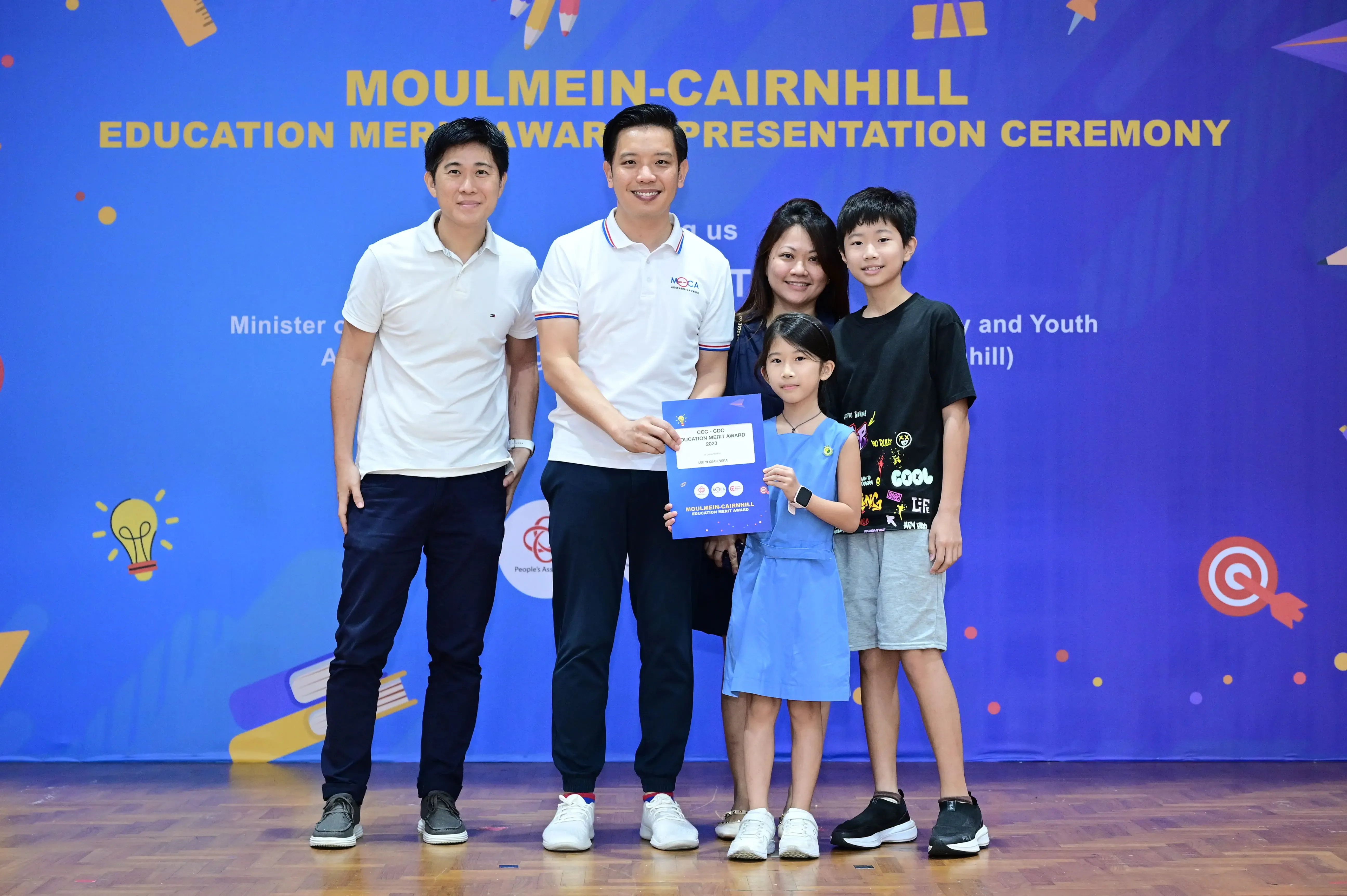 Five people pose at the Moulmein-Cairnhill Education Merit Award Presentation Ceremony, with a girl holding a blue certificate.