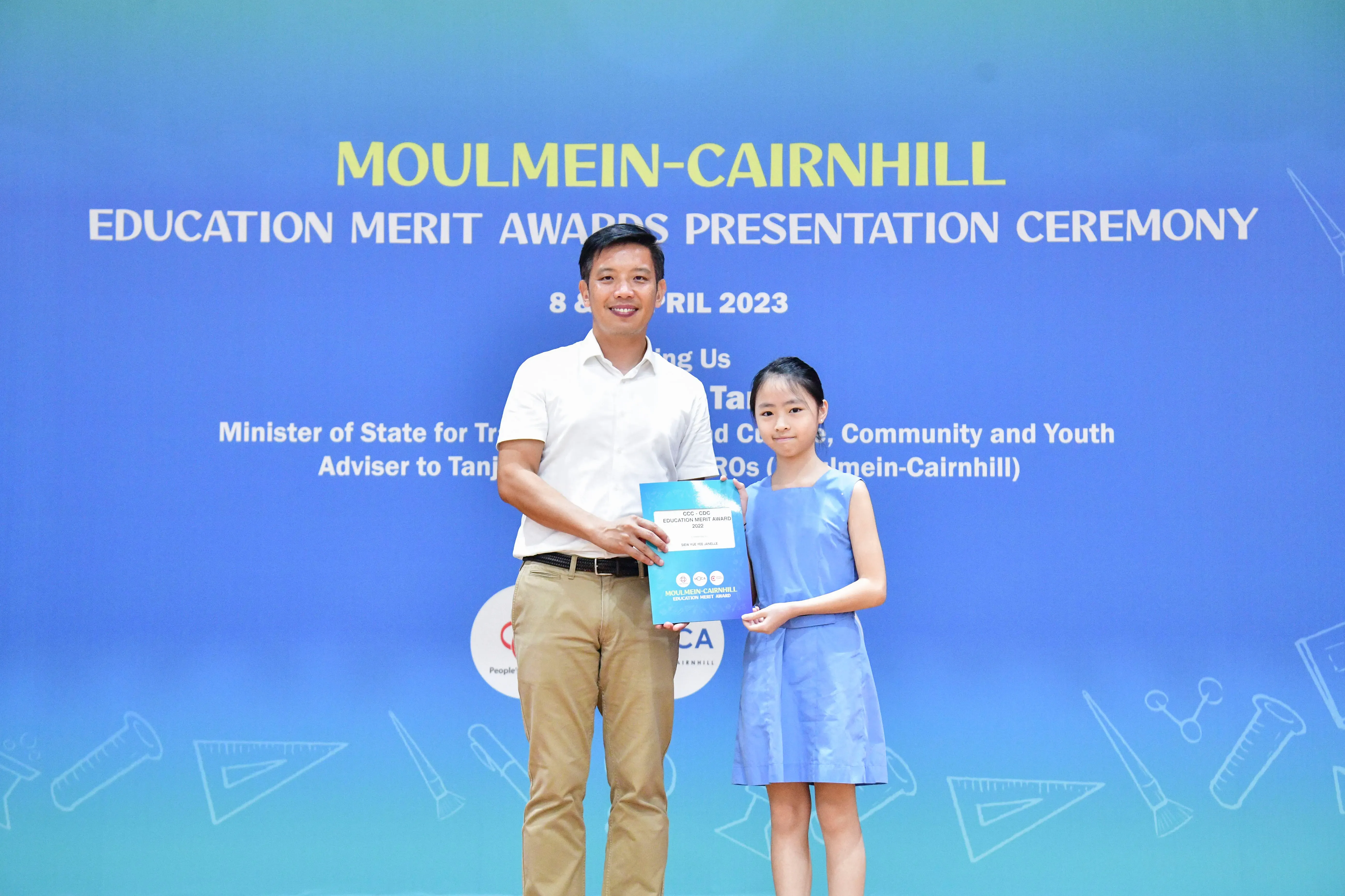 A man and a young girl hold an award certificate at the Moulmein-Cairnhill Education Merit Awards Ceremony, April 2023.