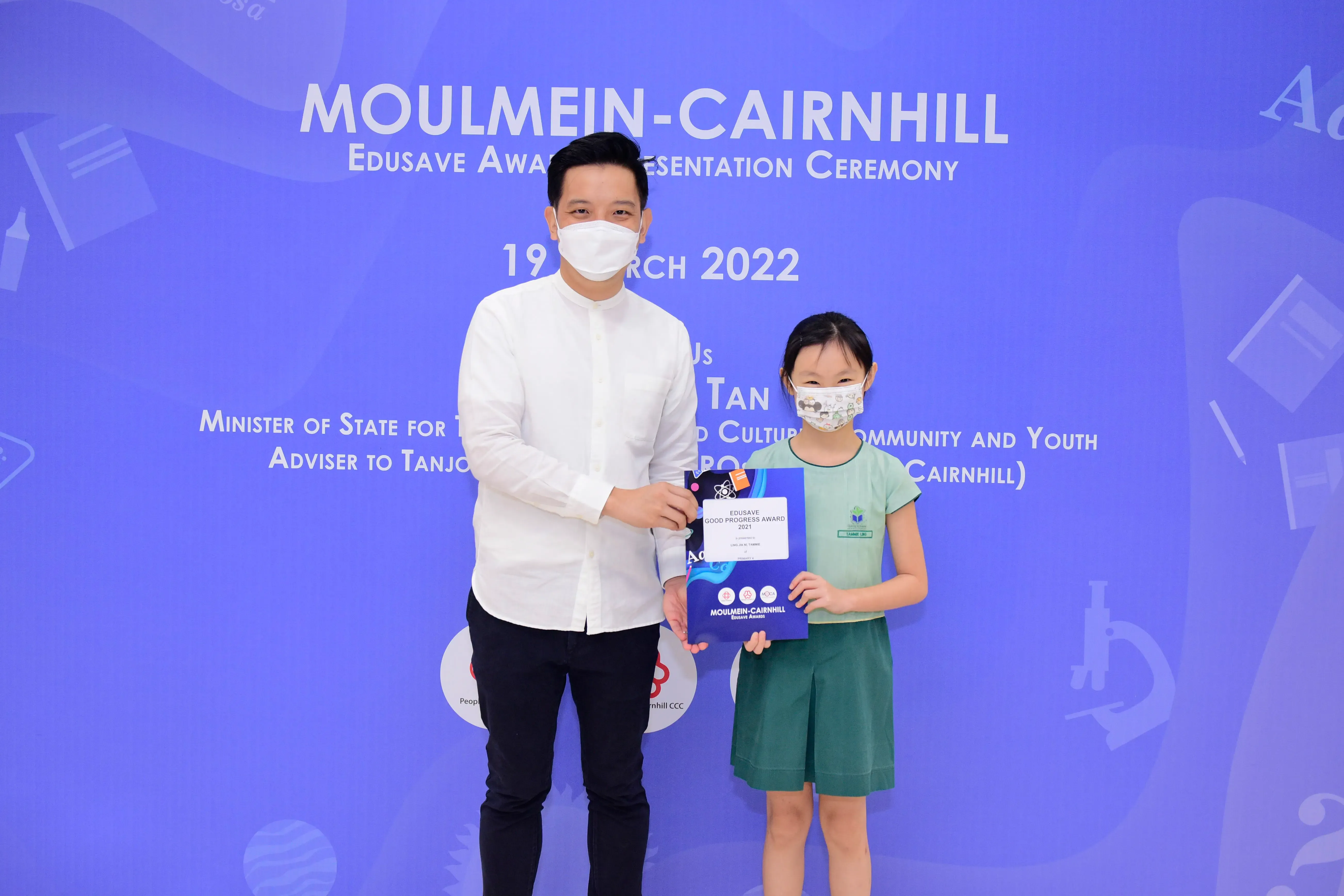 A man and a young girl wearing masks hold an Edusave award certificate at the Moulmein-Cairnhill ceremony on 19 March 2022.