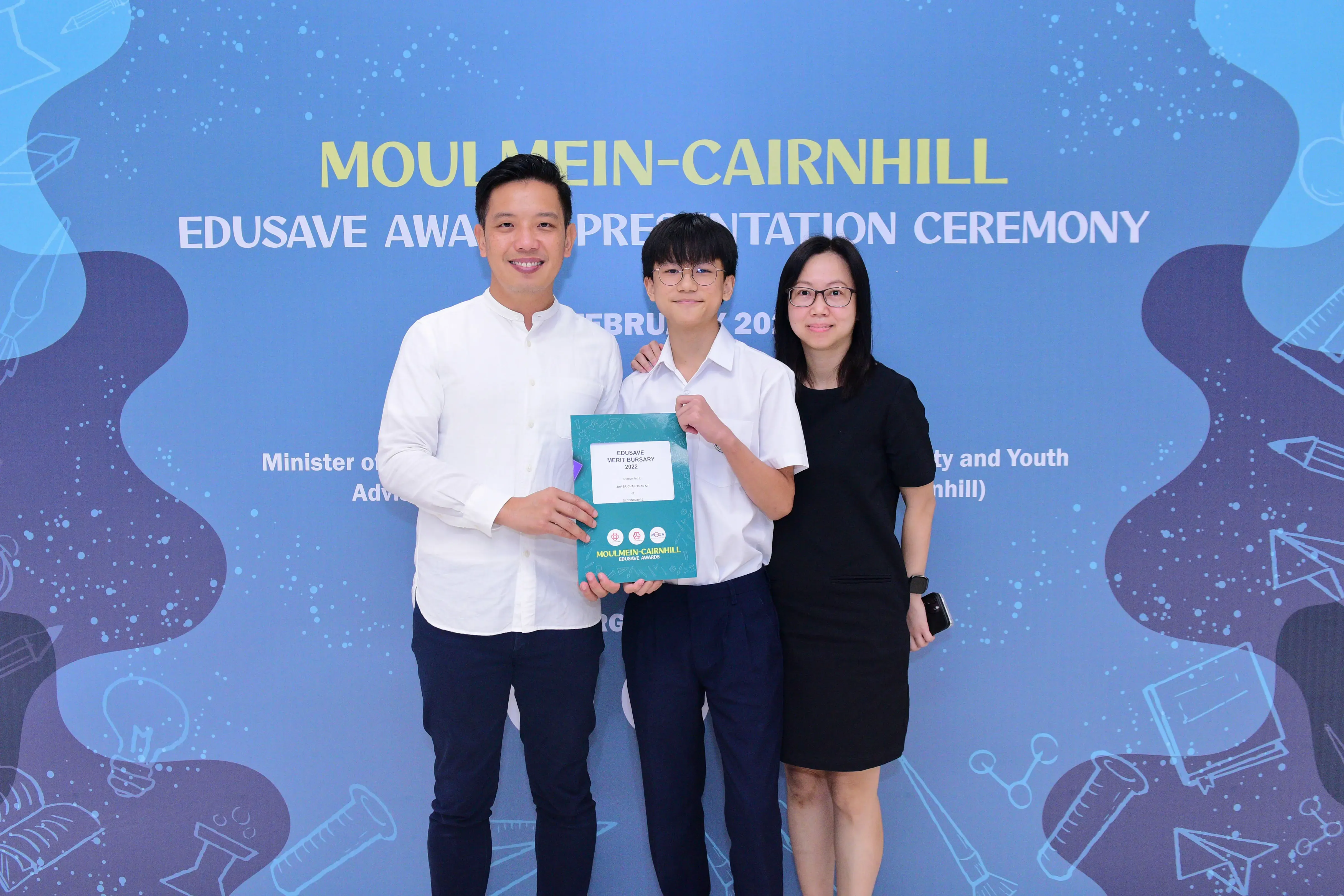 Three people pose holding an Edusave Merit Bursary certificate at the Moulmein-Cairnhill Awards Presentation Ceremony.