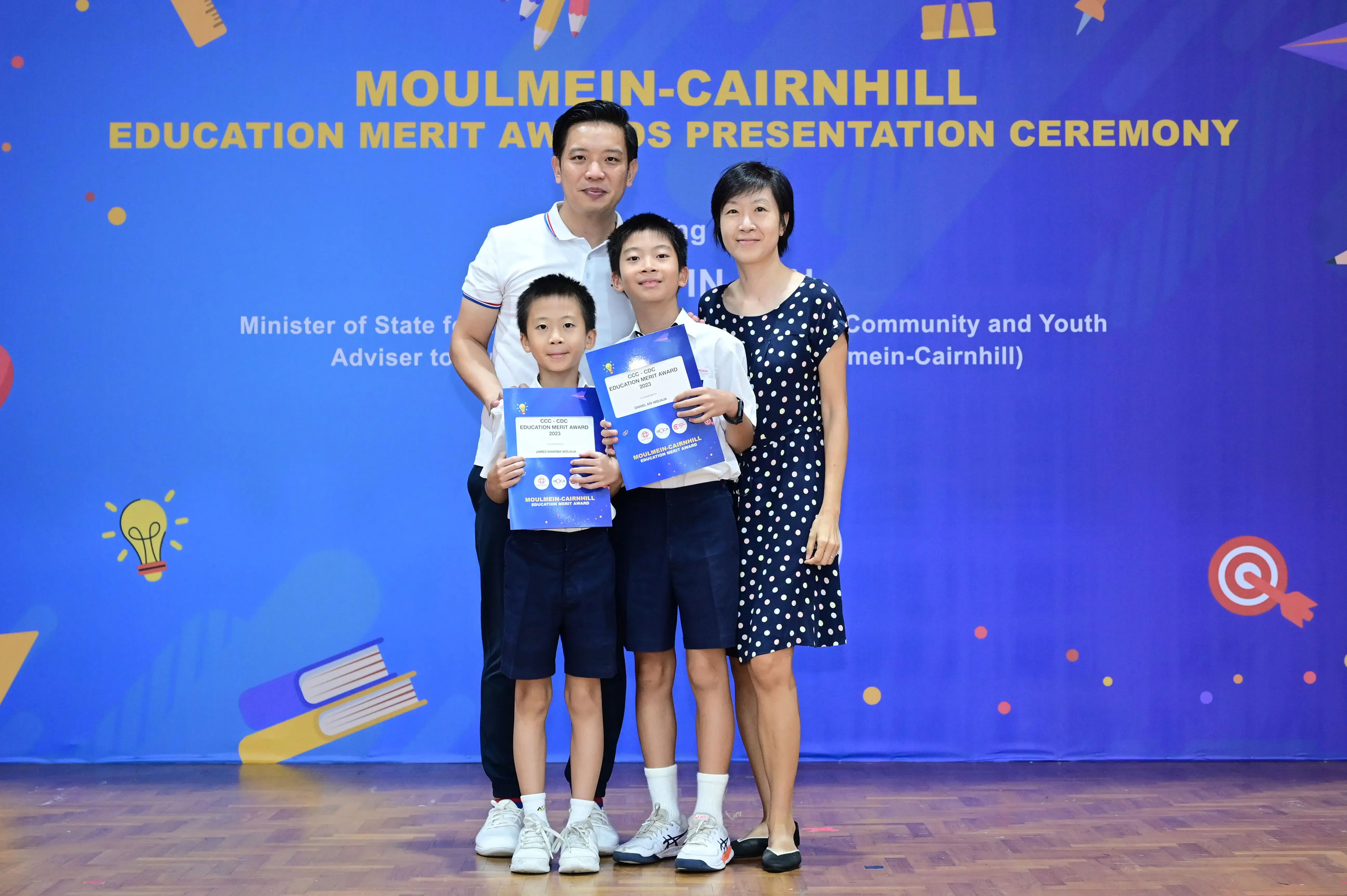 Family of four posing at Moulmein-Cairnhill Education Merit Awards Presentation Ceremony, two boys holding award certificates.