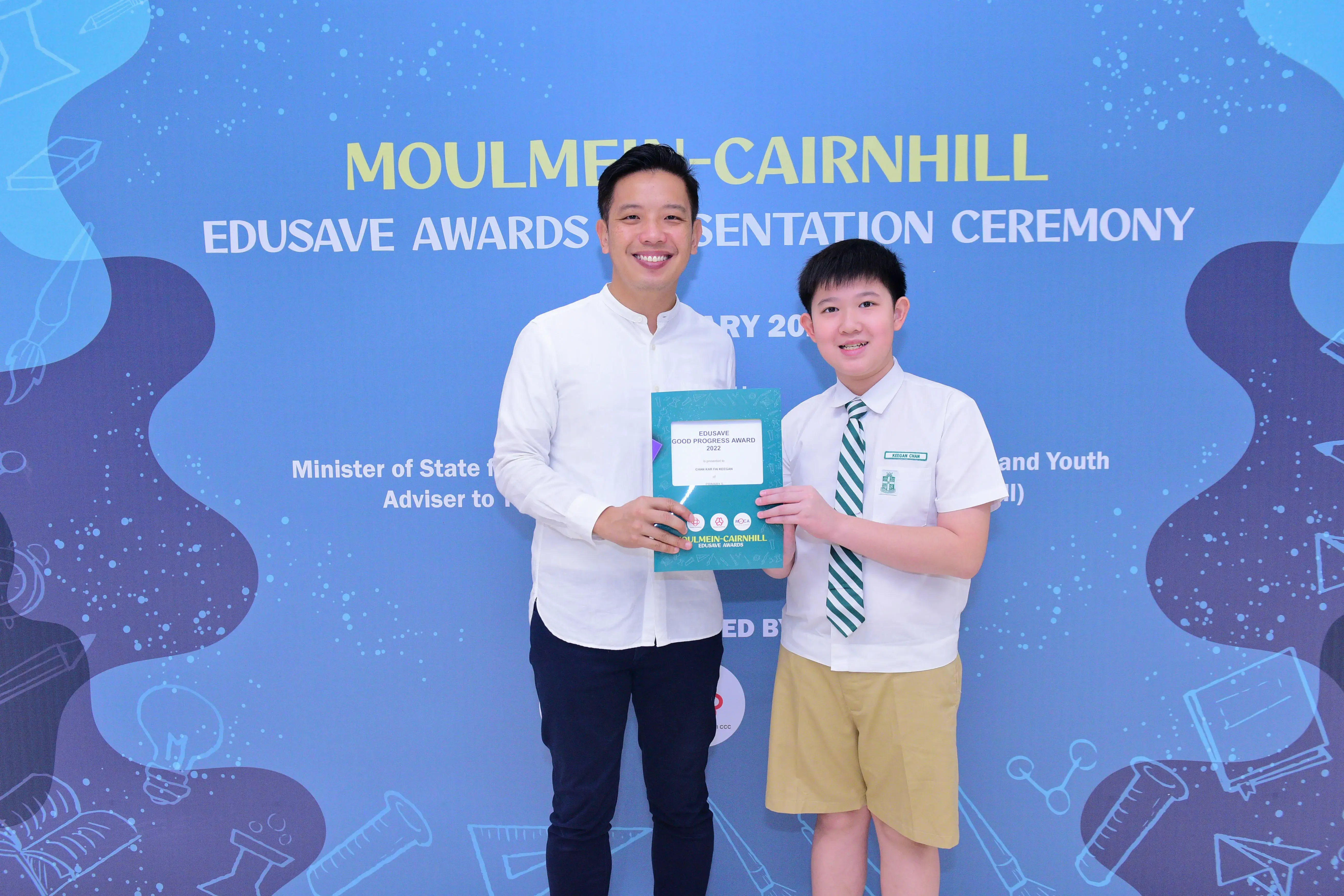 Man and young boy in school uniform hold an Edusave Good Progress Award certificate at Moulmein-Cairnhill ceremony.