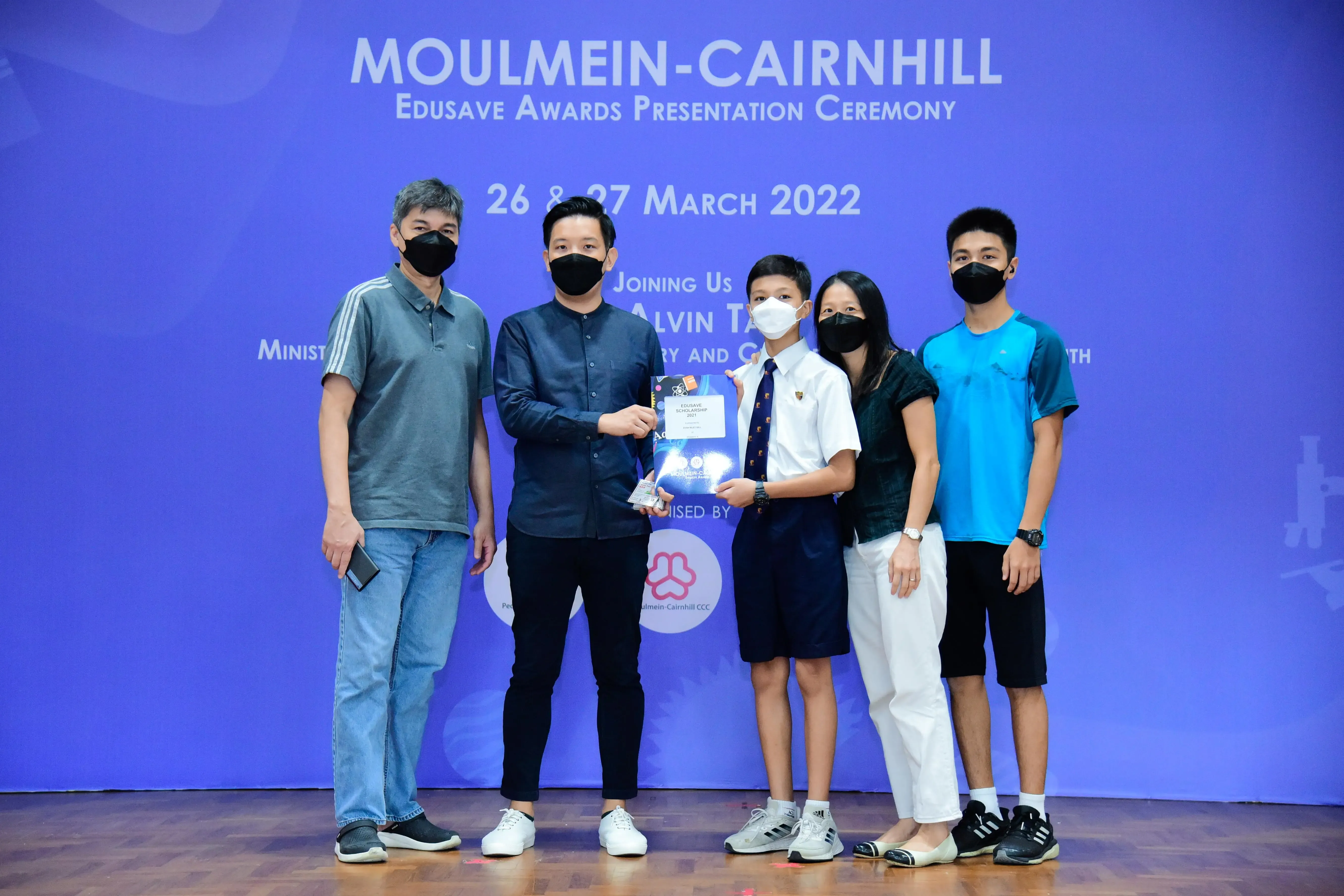 Five masked people pose on stage at the Moulmein-Cairnhill Edusave Awards Presentation Ceremony, March 2022.