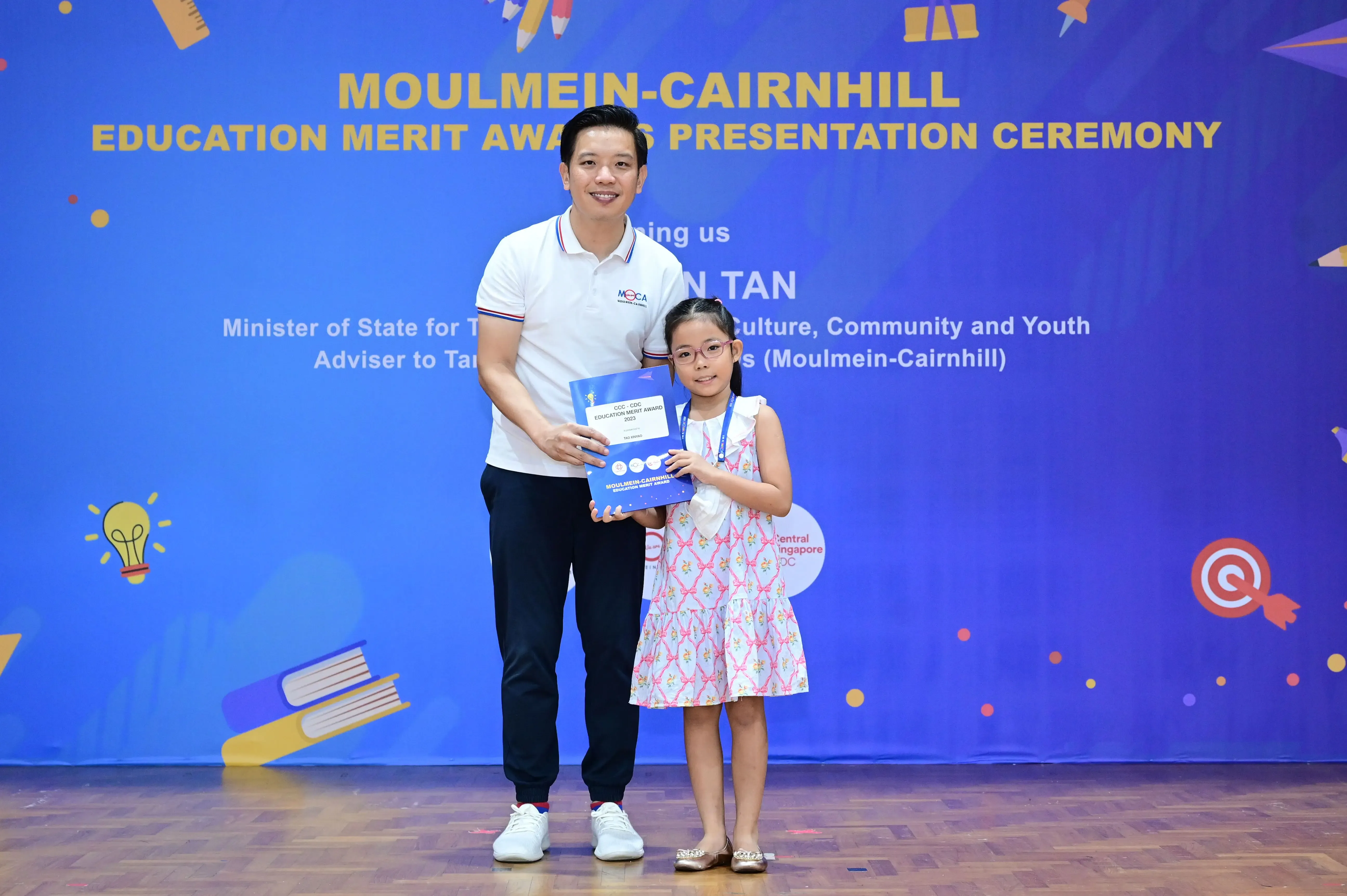 A man and a young girl hold a certificate together at the Moulmein-Cairnhill Education Merit Awards ceremony.