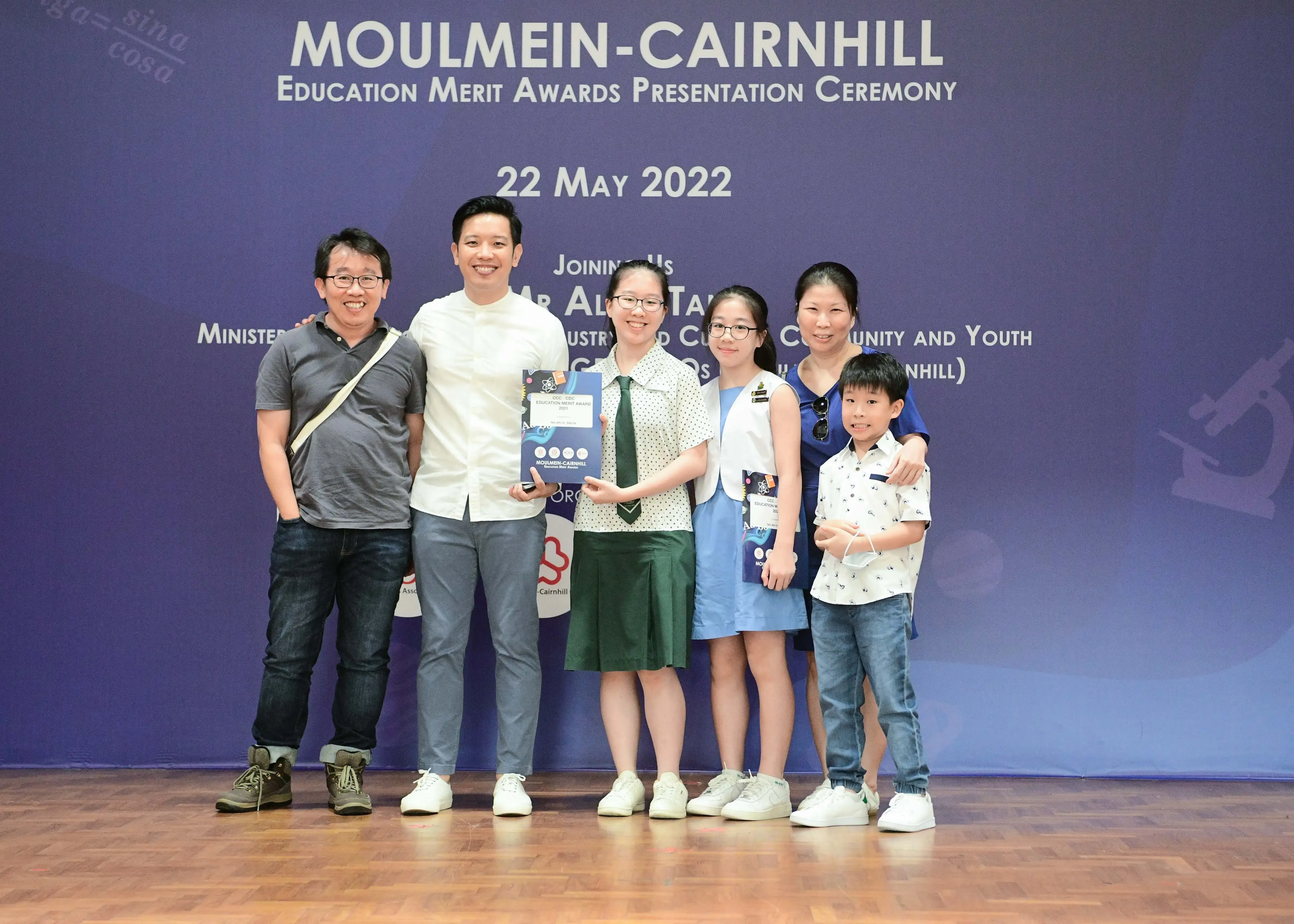 Six people pose in front of the Moulmein-Cairnhill Education Merit Awards banner dated 22 May 2022.