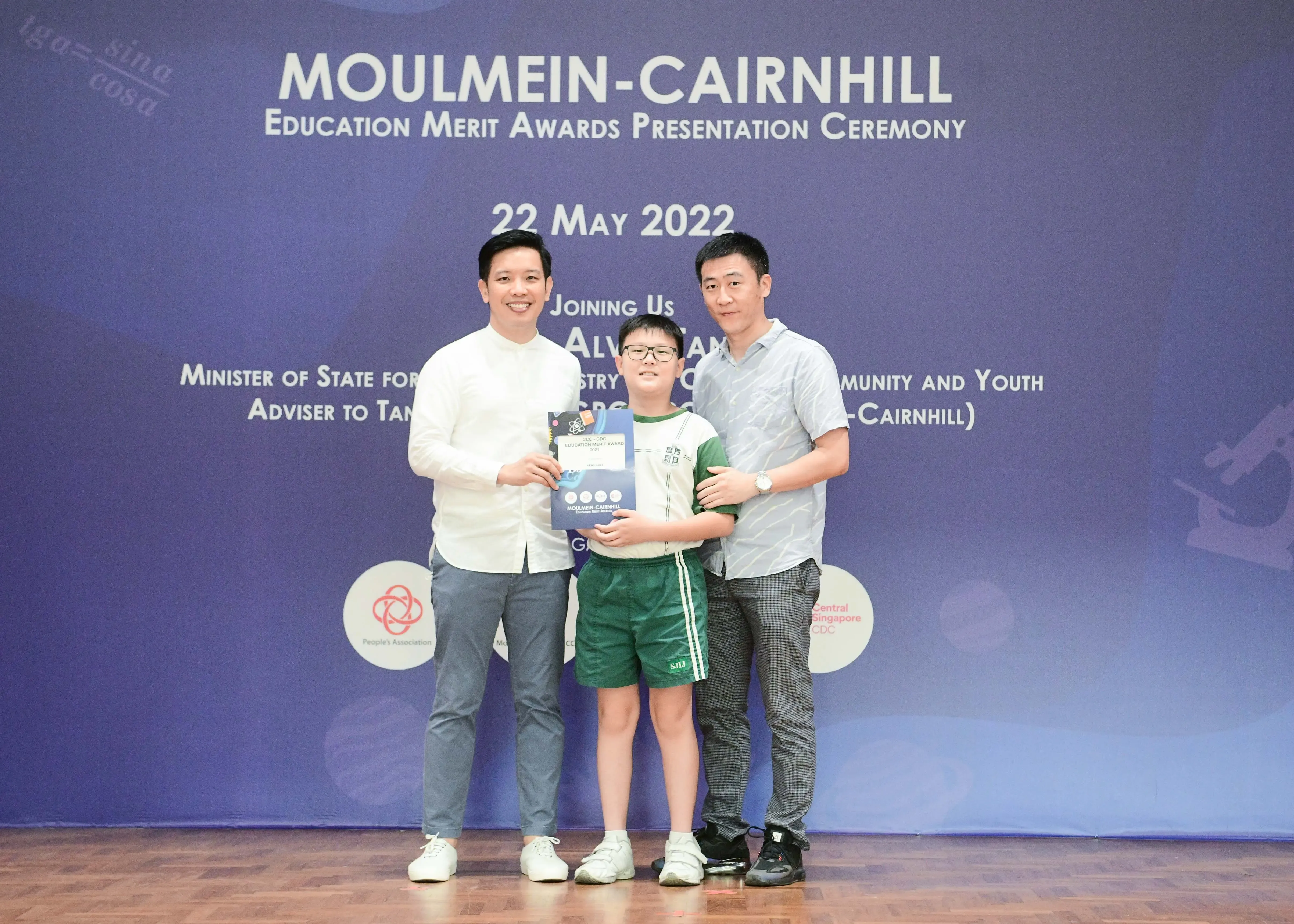 Two men and a boy holding an award booklet pose at the Moulmein-Cairnhill Education Merit Awards ceremony on 22 May 2022.