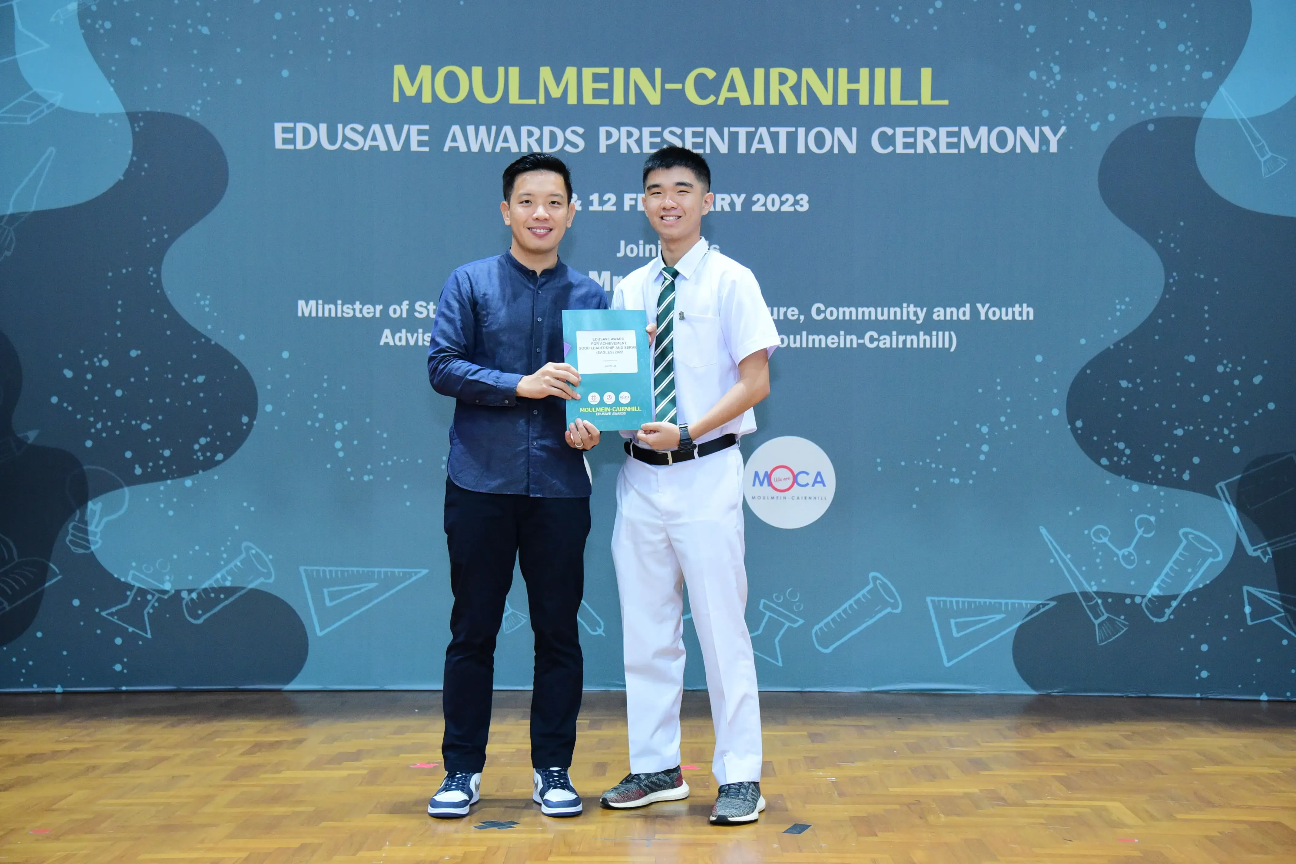Two men hold a certificate together at the Moulmein-Cairnhill Edusave Awards Presentation Ceremony 2023.