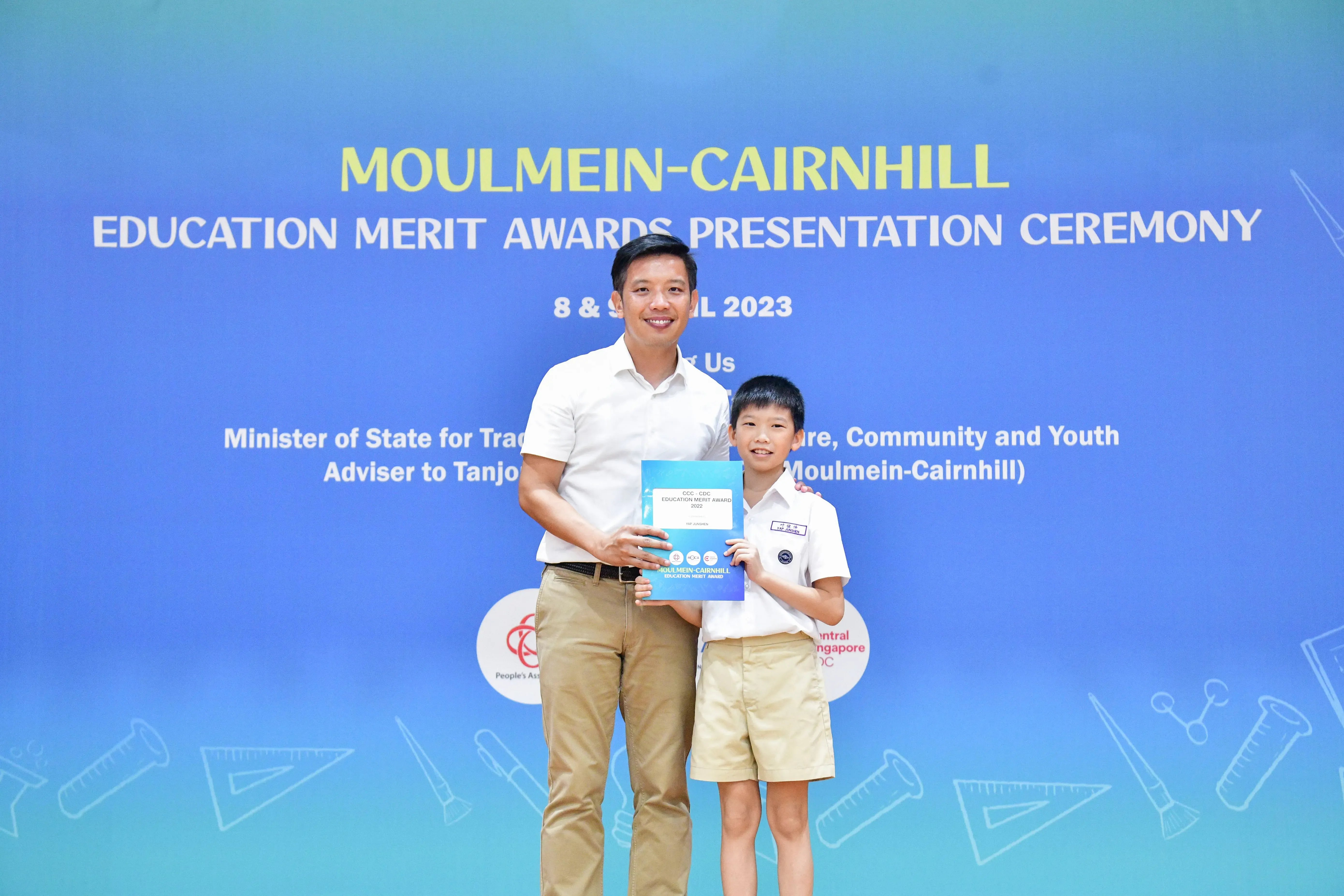 A man and a young boy in school uniform hold a certificate at the Moulmein-Cairnhill Education Merit Awards 2023.