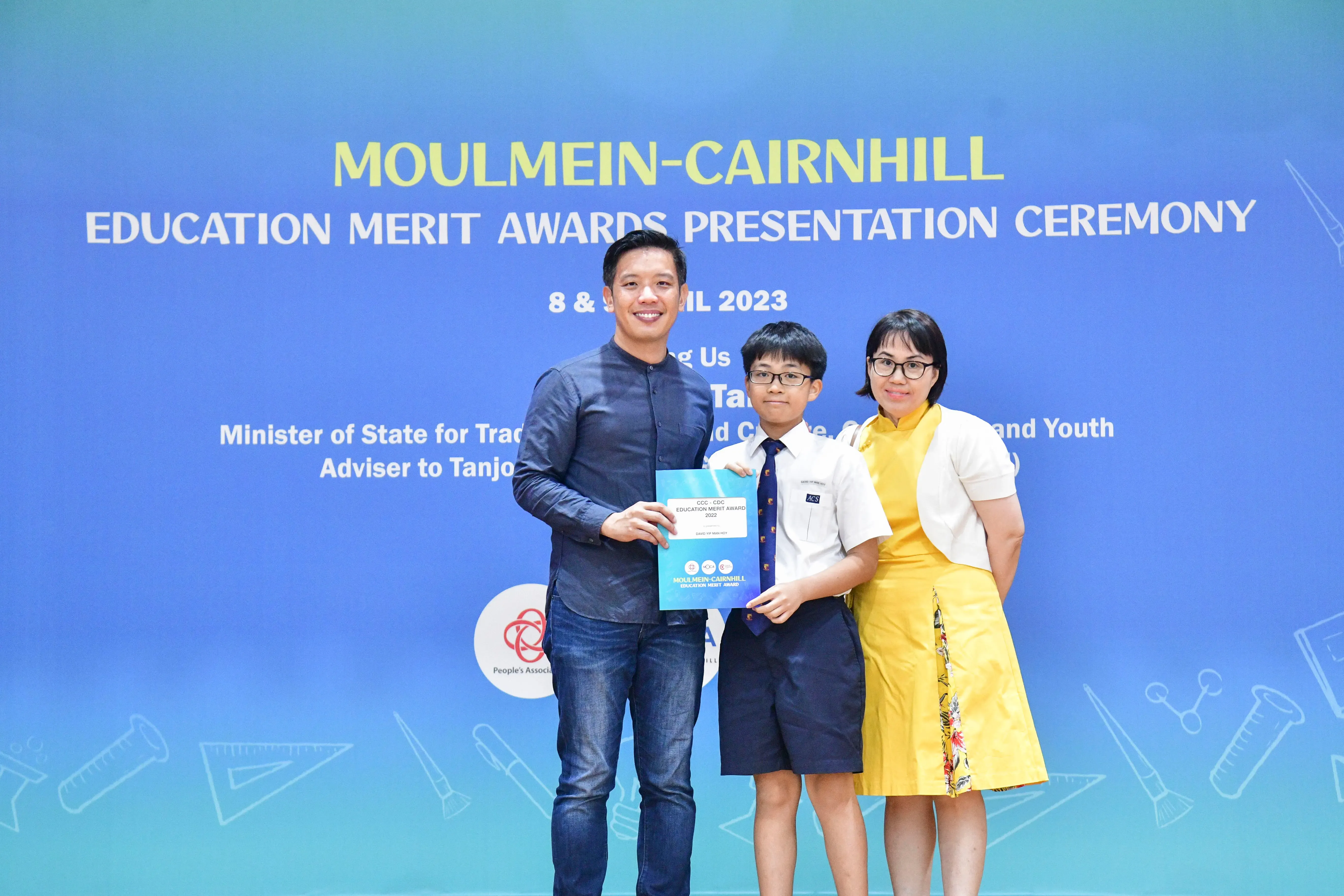 A man, a boy in school uniform, and a woman pose holding an award at the Moulmein-Cairnhill Education Merit Awards 2023.