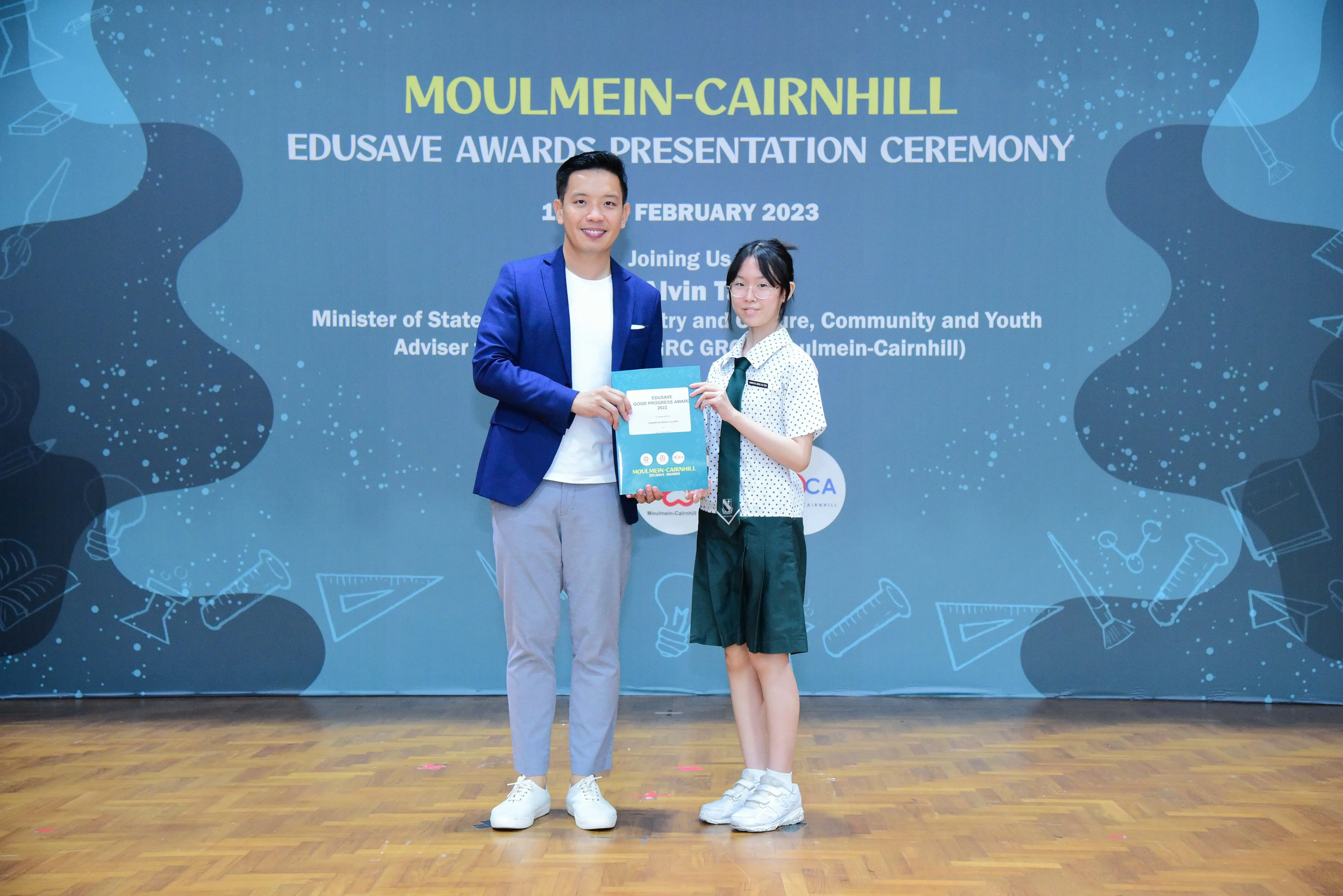 A man in a blue blazer and a girl in school uniform hold an award at the Moulmein-Cairnhill Edusave Awards Ceremony 2023.