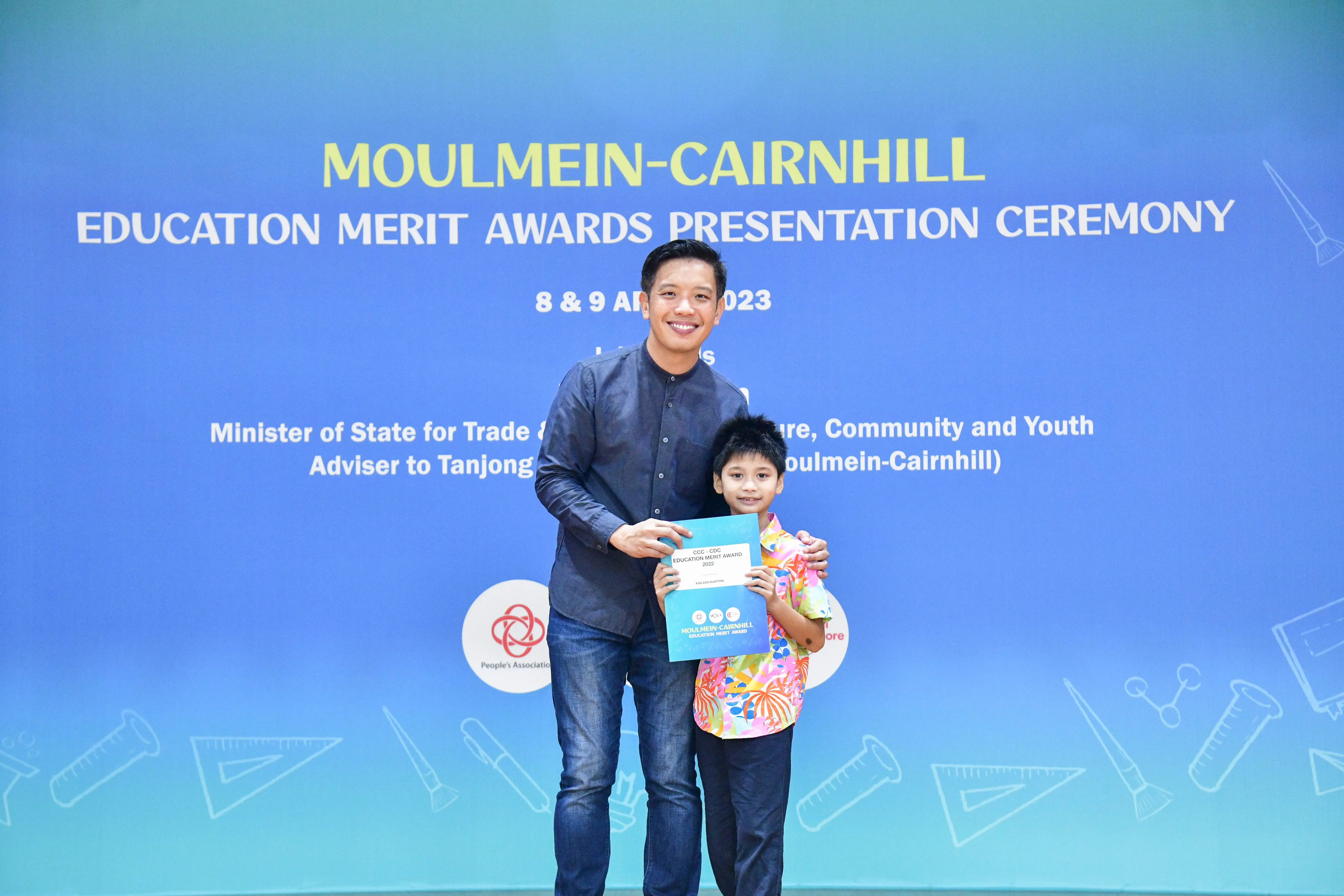 A man and a young boy holding an award certificate at the Moulmein-Cairnhill Education Merit Awards Ceremony 2023.