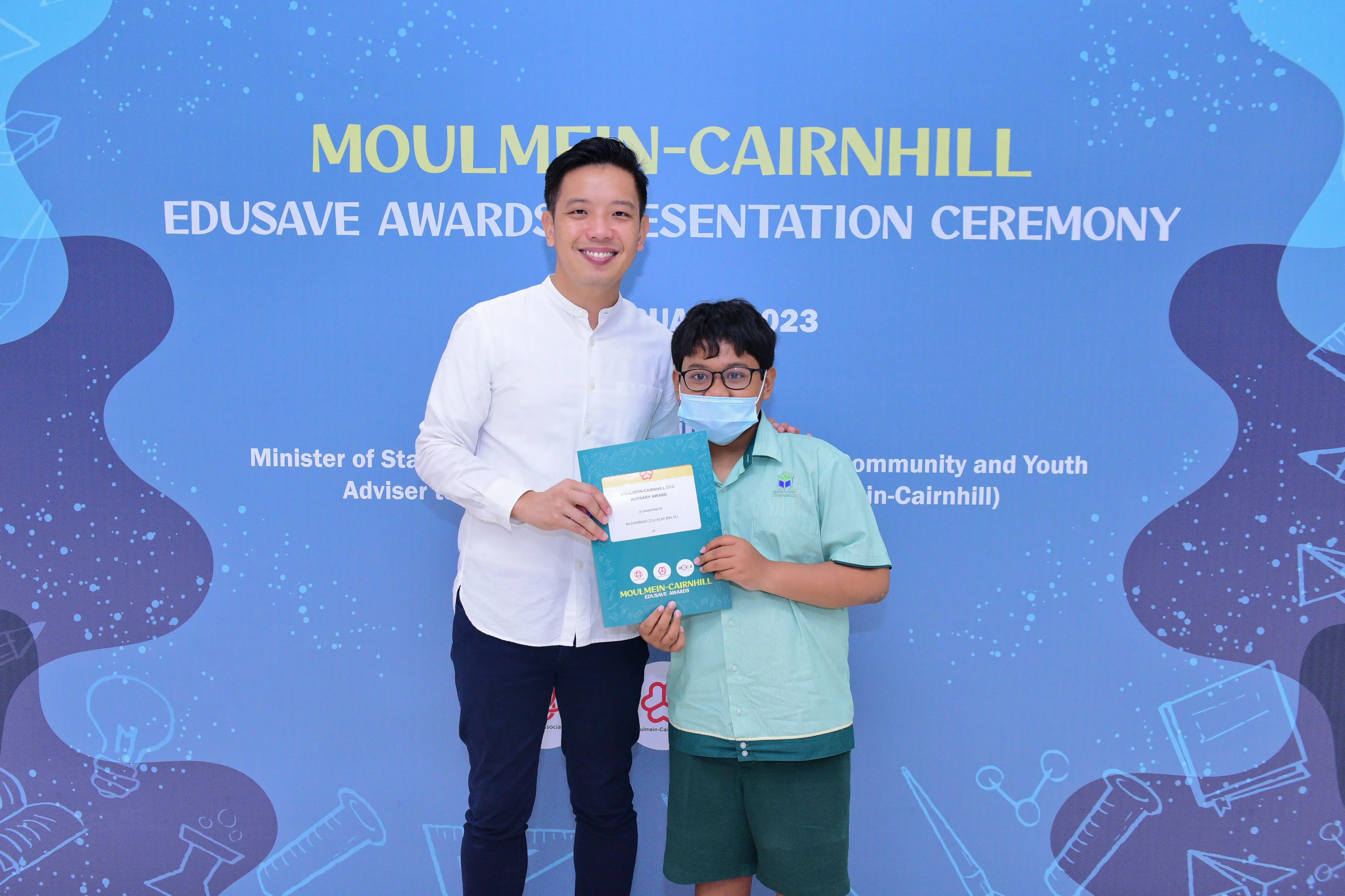 A man and a masked boy hold a certificate at the Moulmein-Cairnhill Edusave Awards Presentation Ceremony 2023.