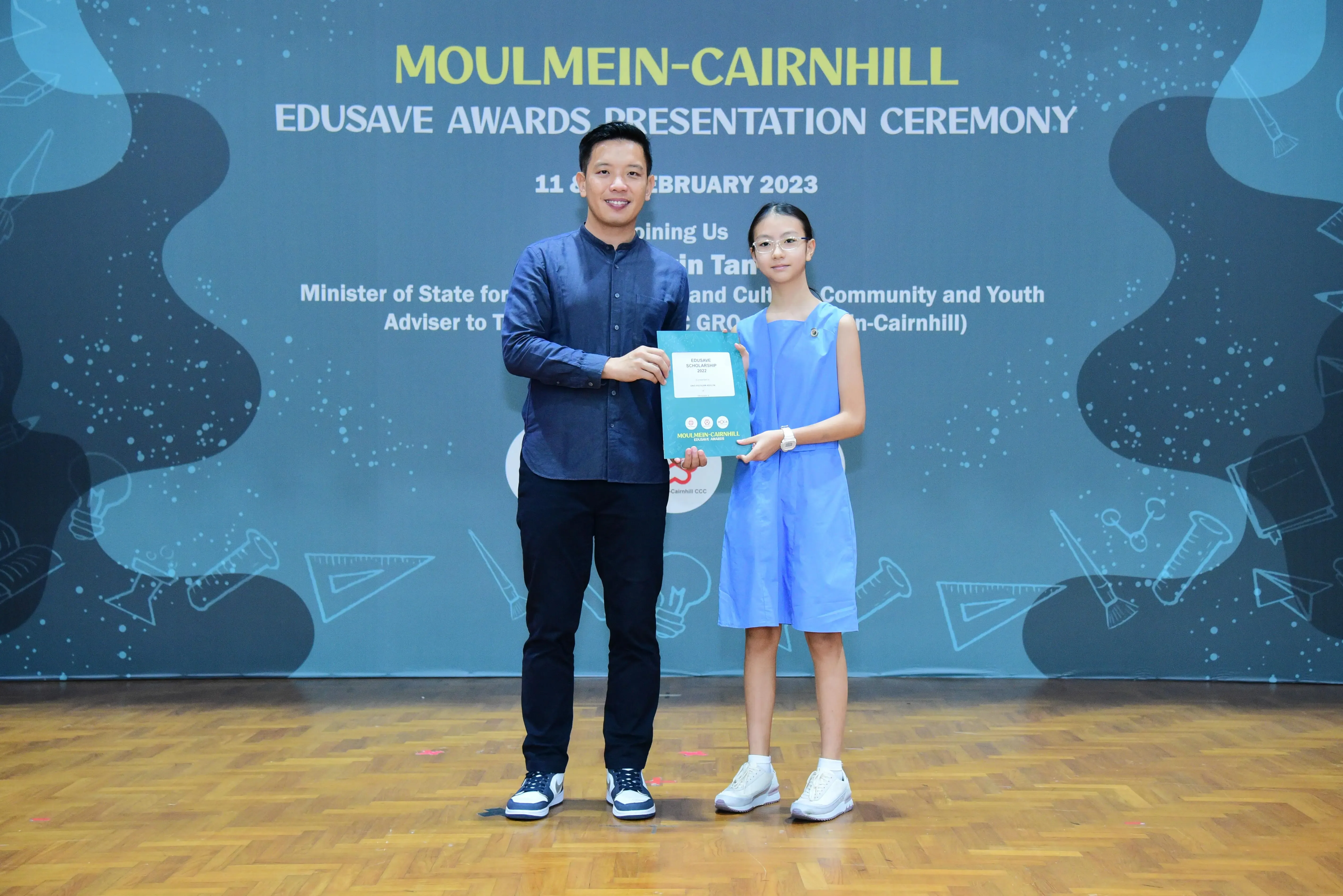 A man and a young girl hold a certificate together at the Moulmein-Cairnhill Edusave Awards Ceremony in 2023.