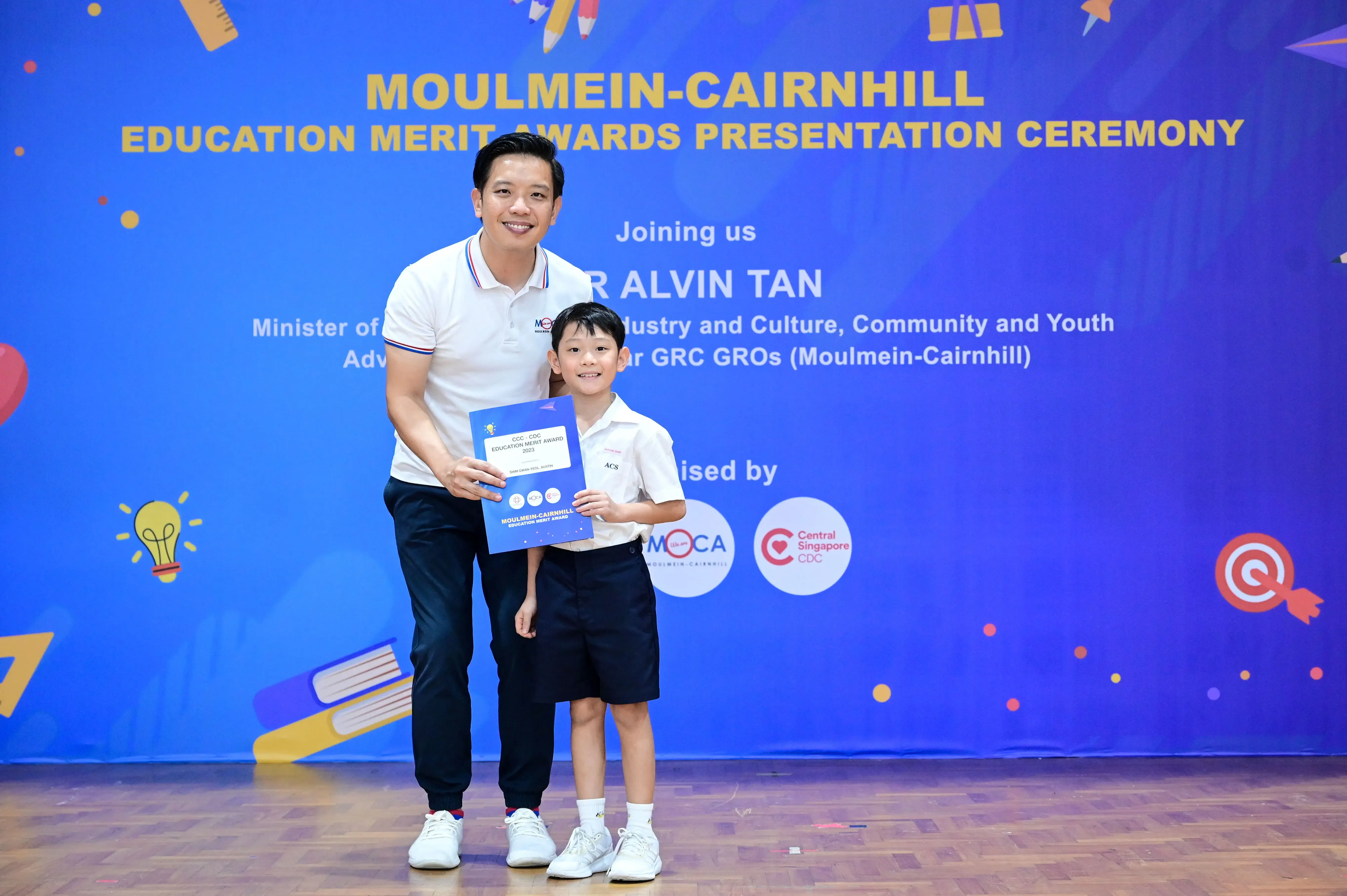 A man and a young boy hold a certificate at the Moulmein-Cairnhill Education Merit Awards Presentation Ceremony.