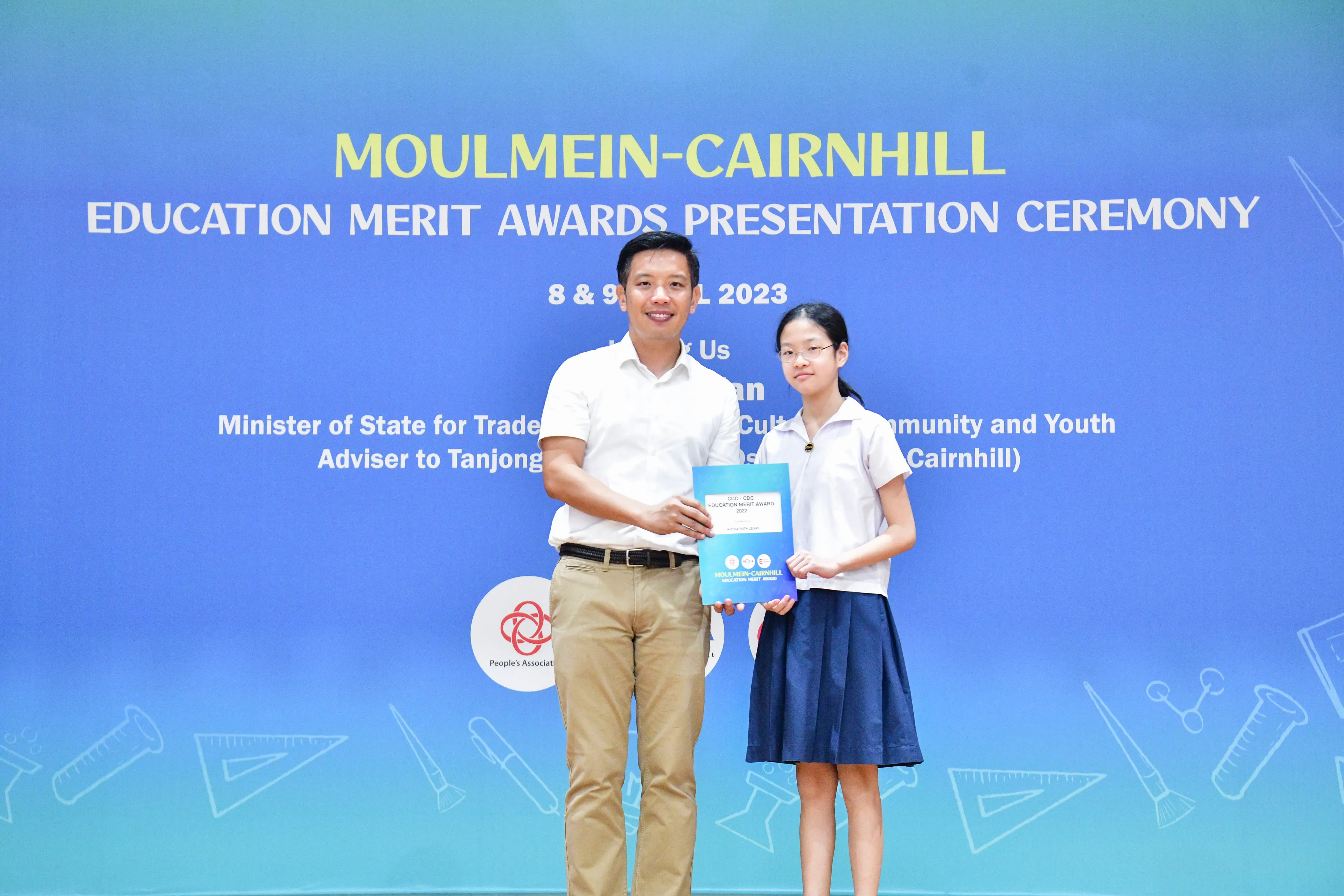 A man and a young girl hold an award certificate at the Moulmein-Cairnhill Education Merit Awards Ceremony 2023.
