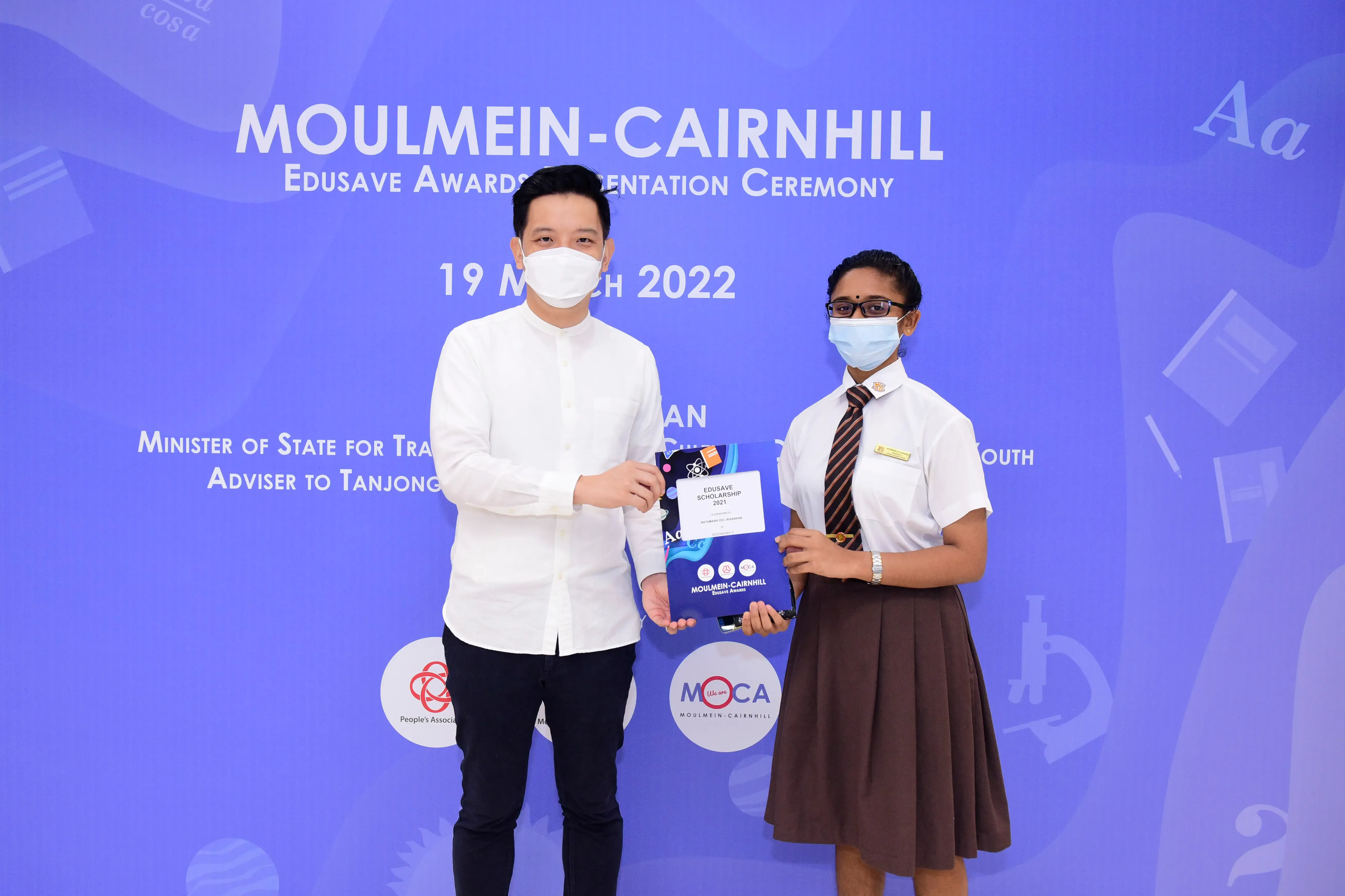 Two masked people hold an Edusave Scholarship folder at the Moulmein-Cairnhill Awards Ceremony on 19 March 2022.