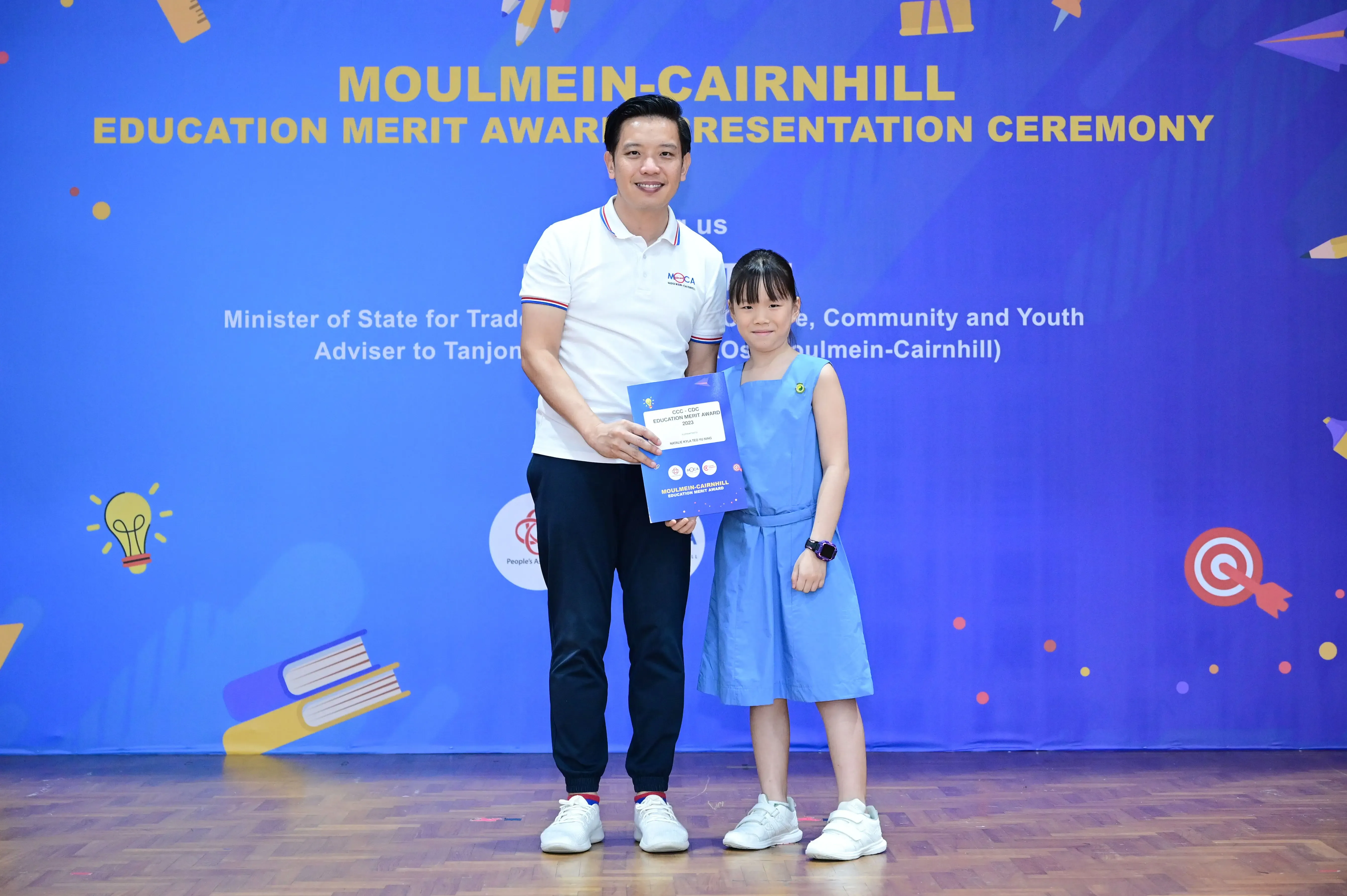 A man and a young girl hold an award certificate at the Moulmein-Cairnhill Education Merit Award Presentation Ceremony.