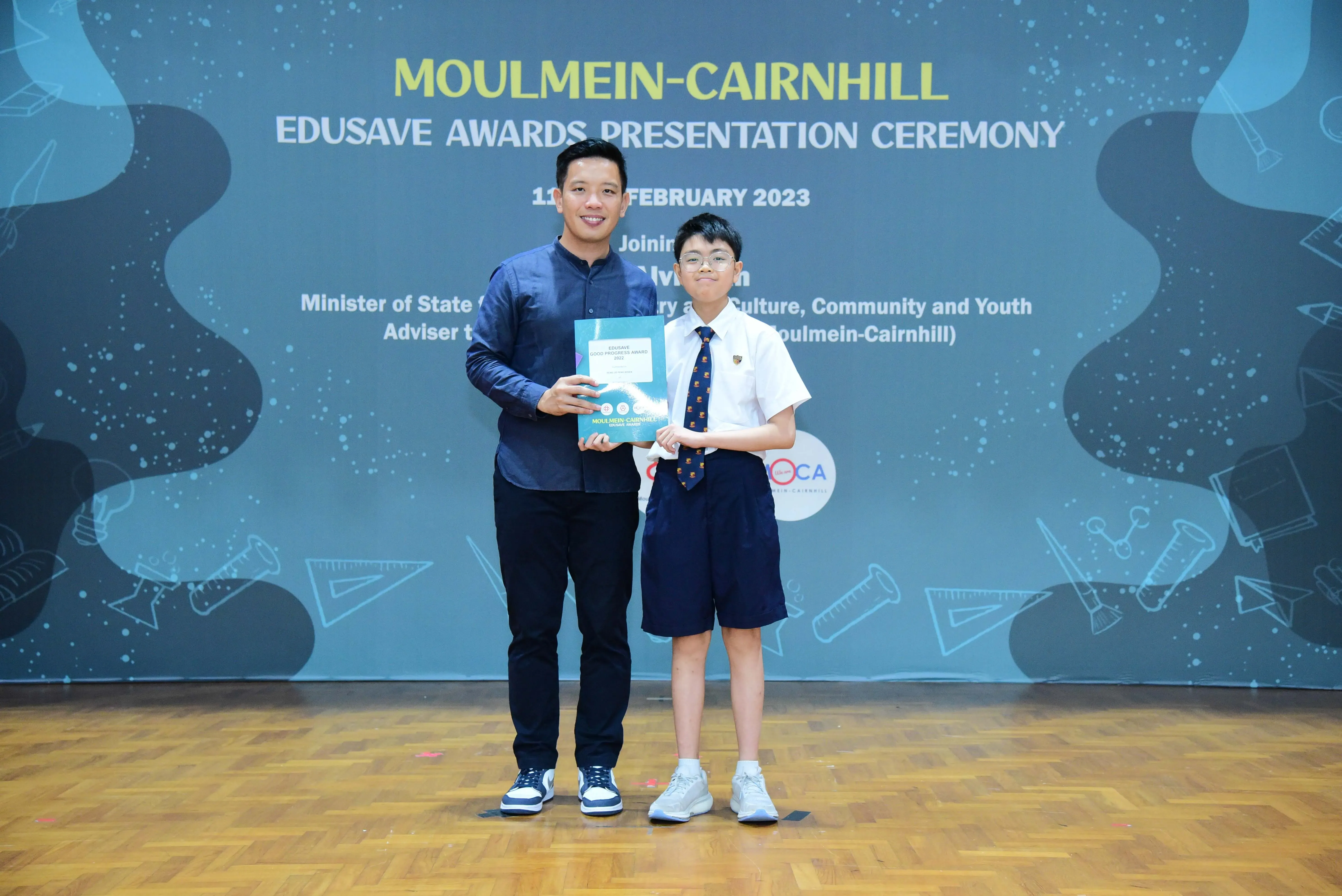 An adult and a young student hold an award certificate at the Moulmein-Cairnhill Edusave Awards Ceremony, February 2023.