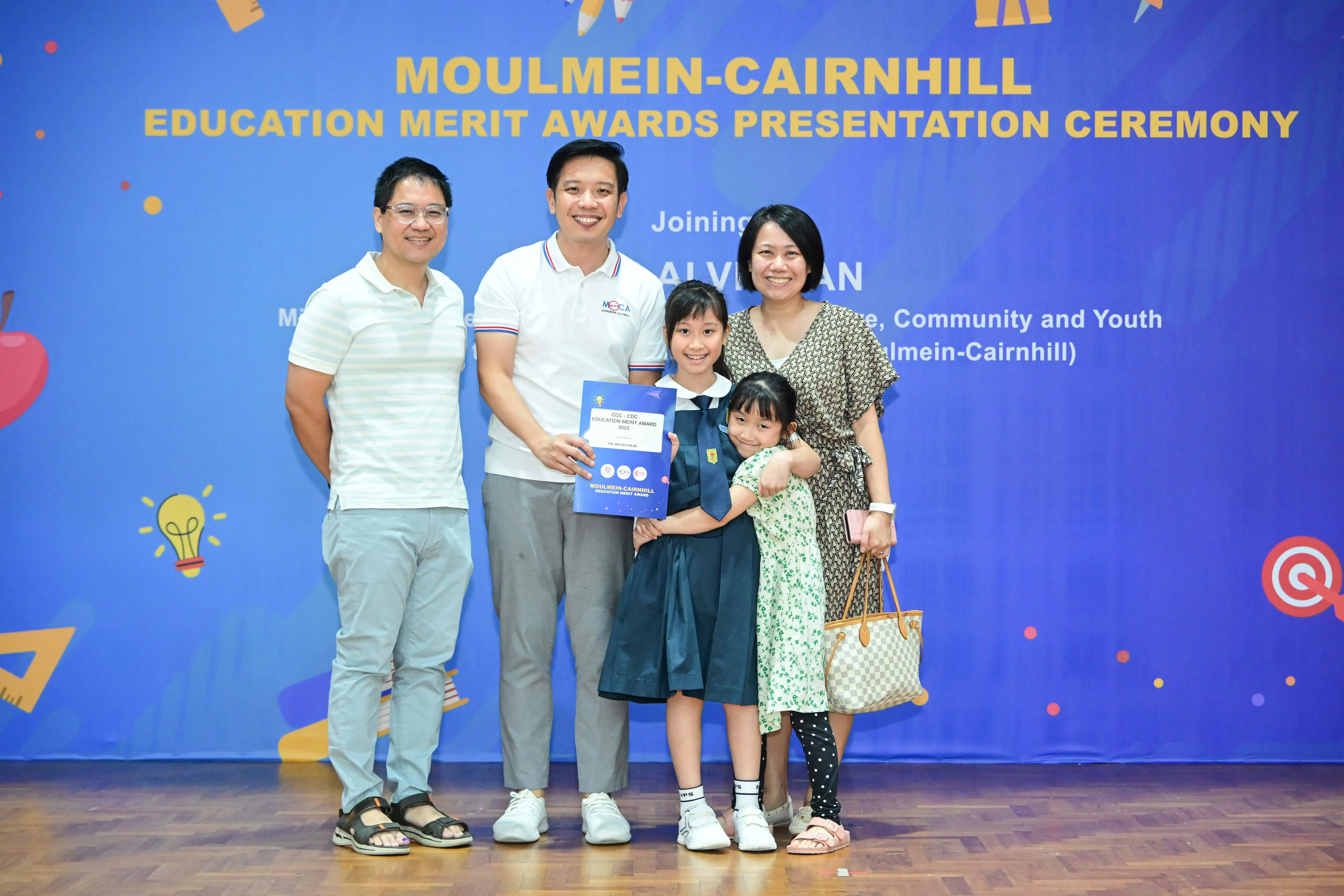 Family of five posing with an award certificate at the Moulmein-Cairnhill Education Merit Awards Presentation Ceremony.