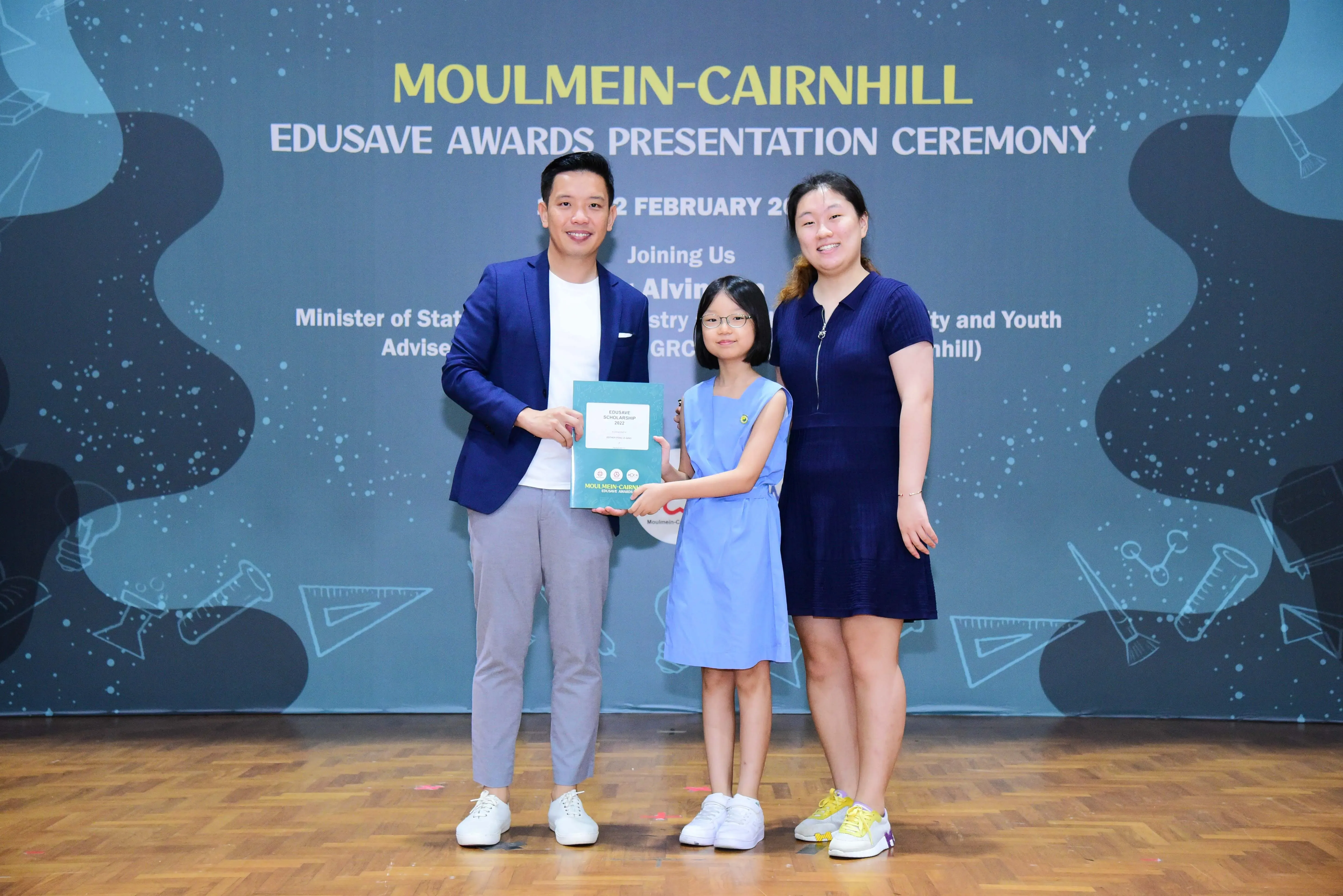 A man, young girl, and woman pose with an award at the Moulmein-Cairnhill Edusave Awards Presentation Ceremony.