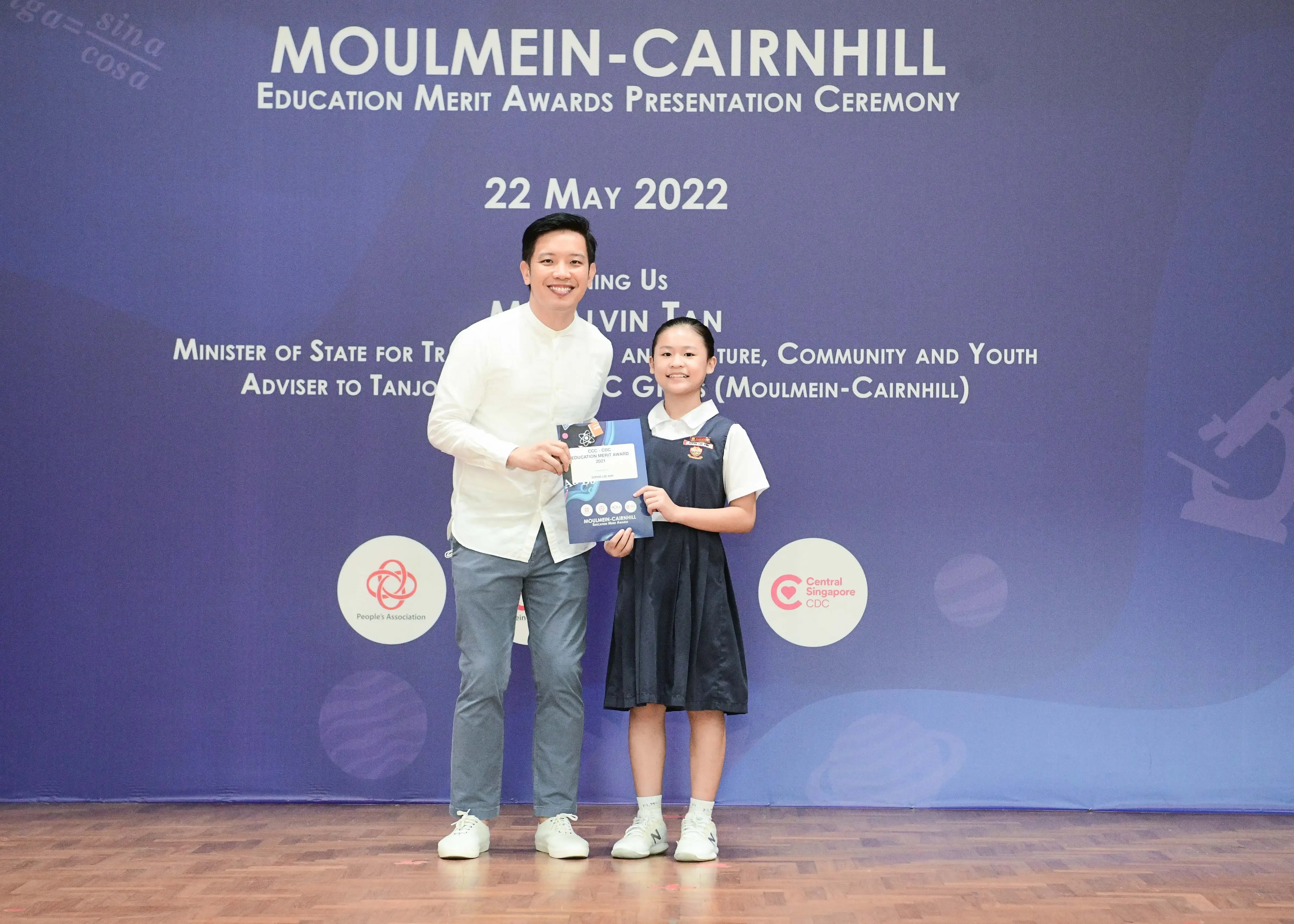 A man and a young girl in school uniform hold an award at the Moulmein-Cairnhill Education Merit Awards Ceremony, May 2022.