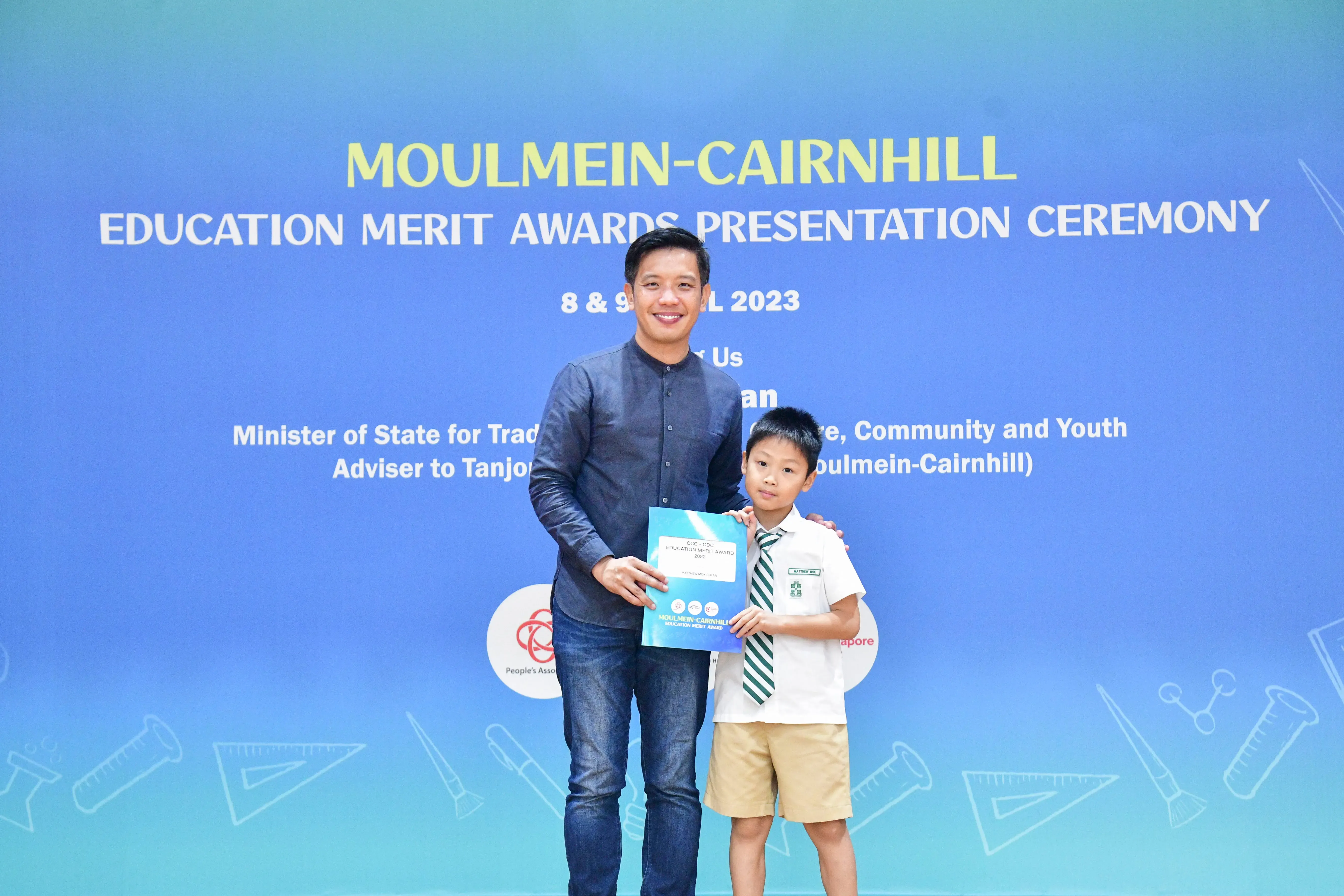 A man and a young boy in school uniform pose holding a certificate at the Moulmein-Cairnhill Education Merit Awards 2023.
