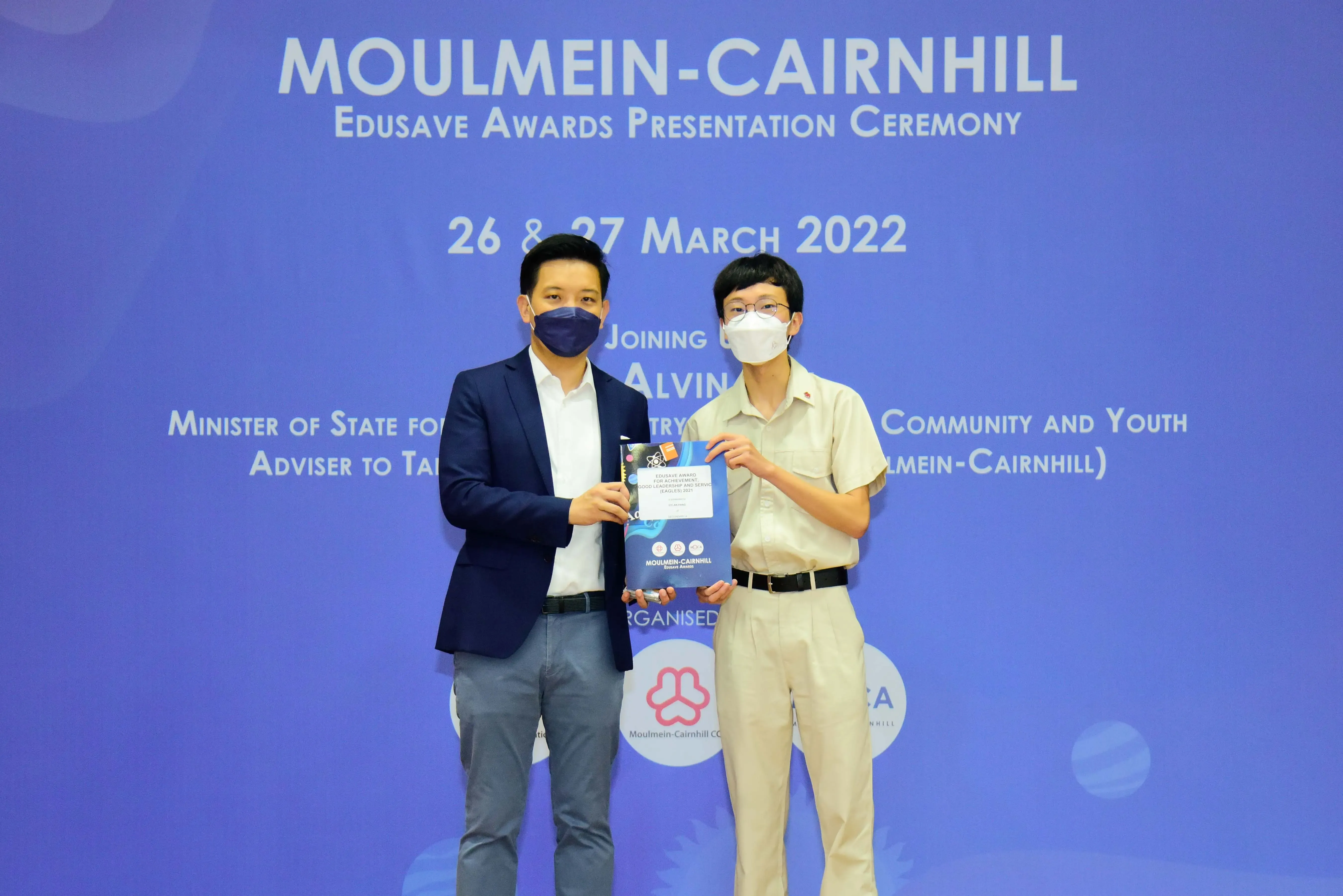 Two masked people hold an award booklet at the Moulmein-Cairnhill Edusave Awards Presentation Ceremony, March 2022.