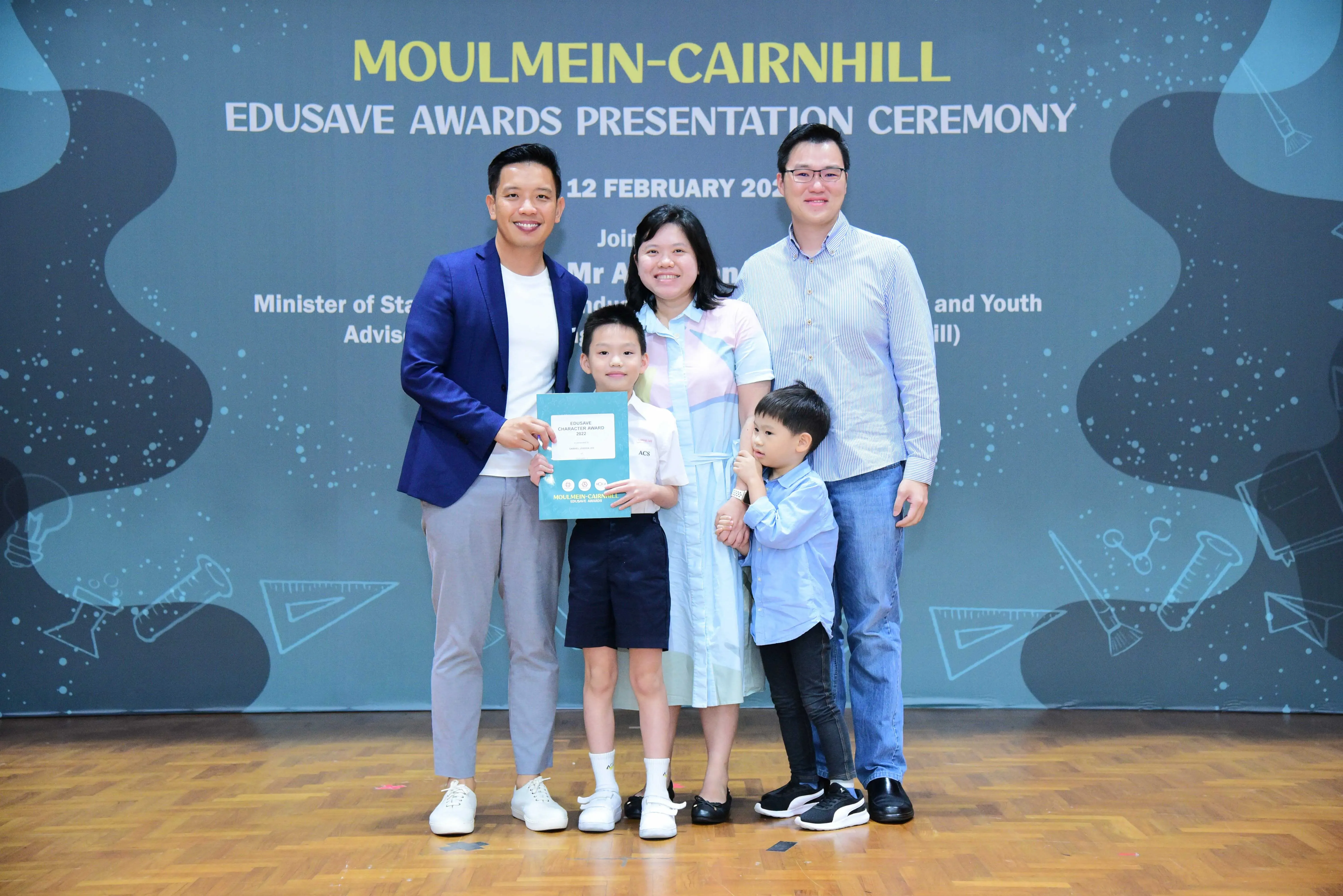 Four adults and two children pose with a certificate at the Moulmein-Cairnhill Edusave Awards Presentation Ceremony.