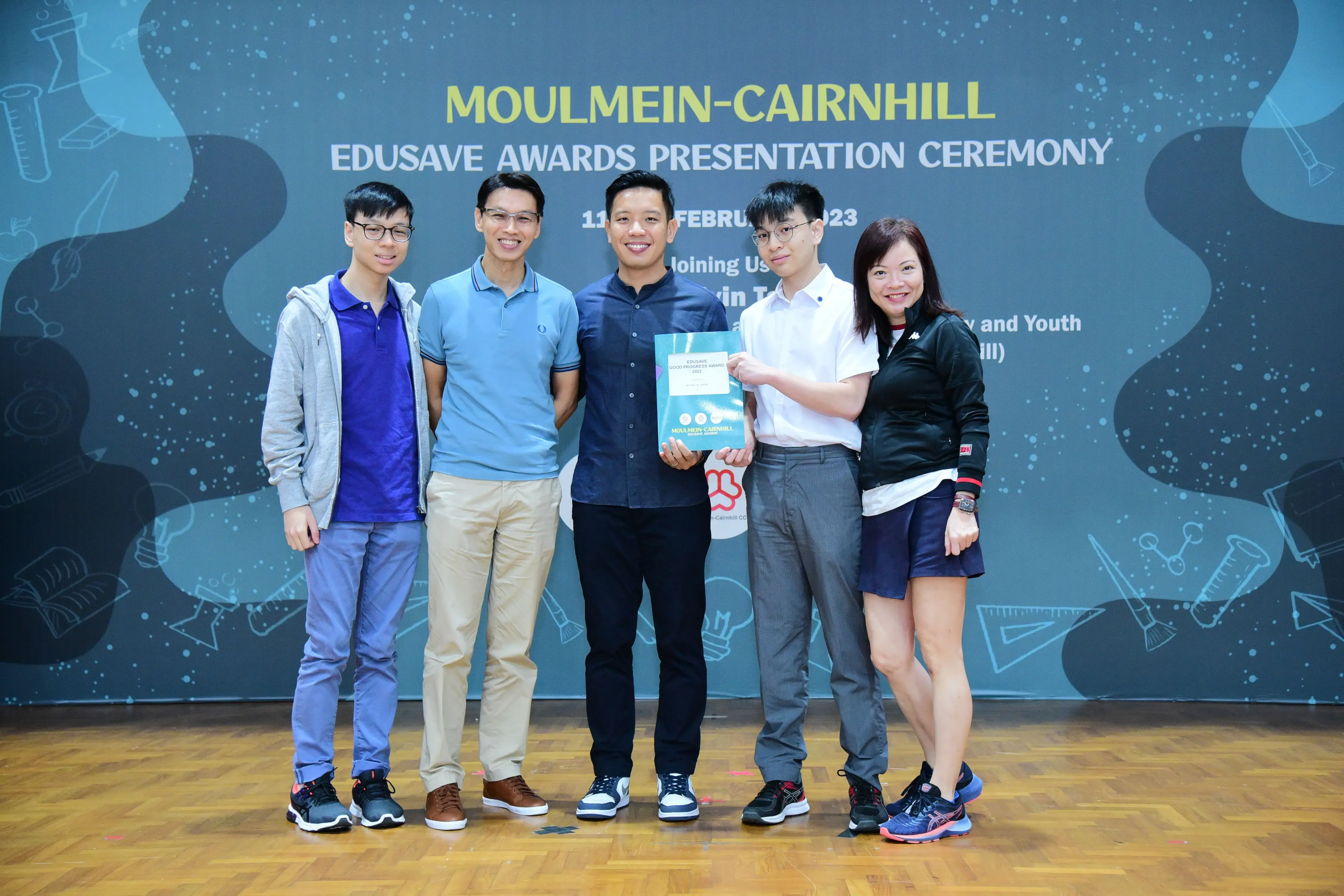 Five people pose smiling at the Moulmein-Cairnhill Edusave Awards Presentation Ceremony, one holding an award certificate.