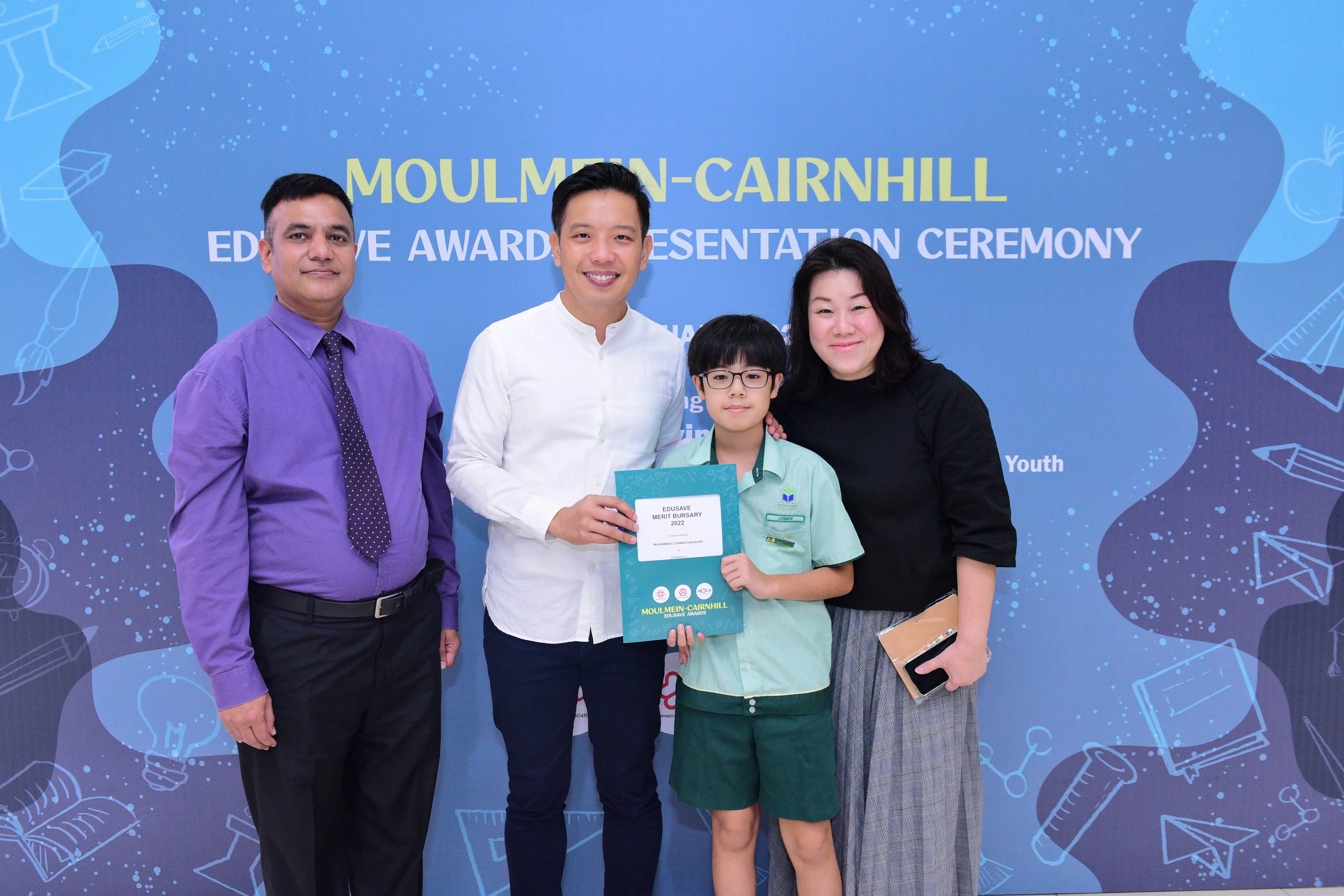Four people pose at the Moulmein-Cairnhill Edusave Awards Presentation Ceremony, a boy holding a certificate.