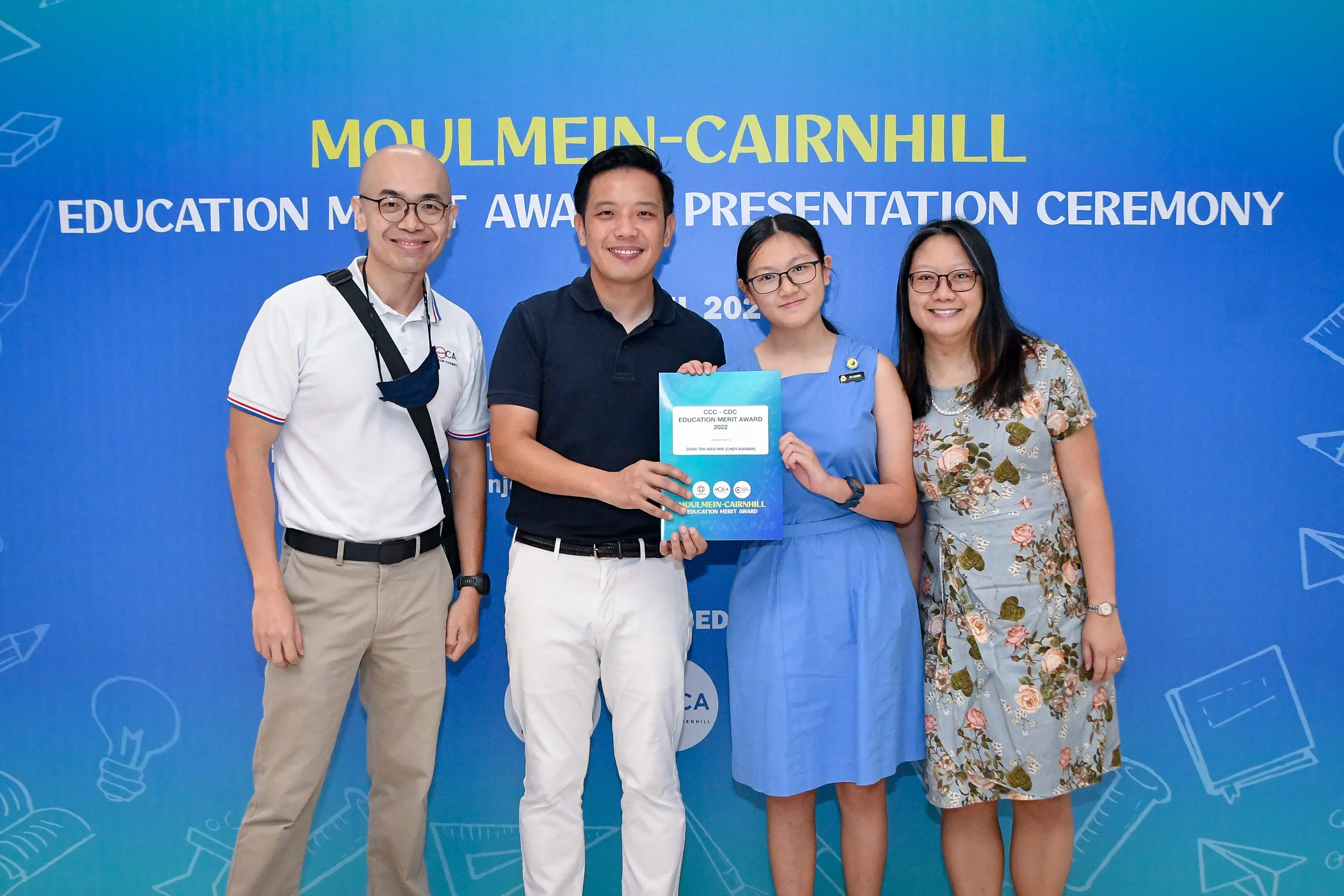 Four people pose together at the Moulmein-Cairnhill Education Merit Award Presentation Ceremony, holding an award certificate.