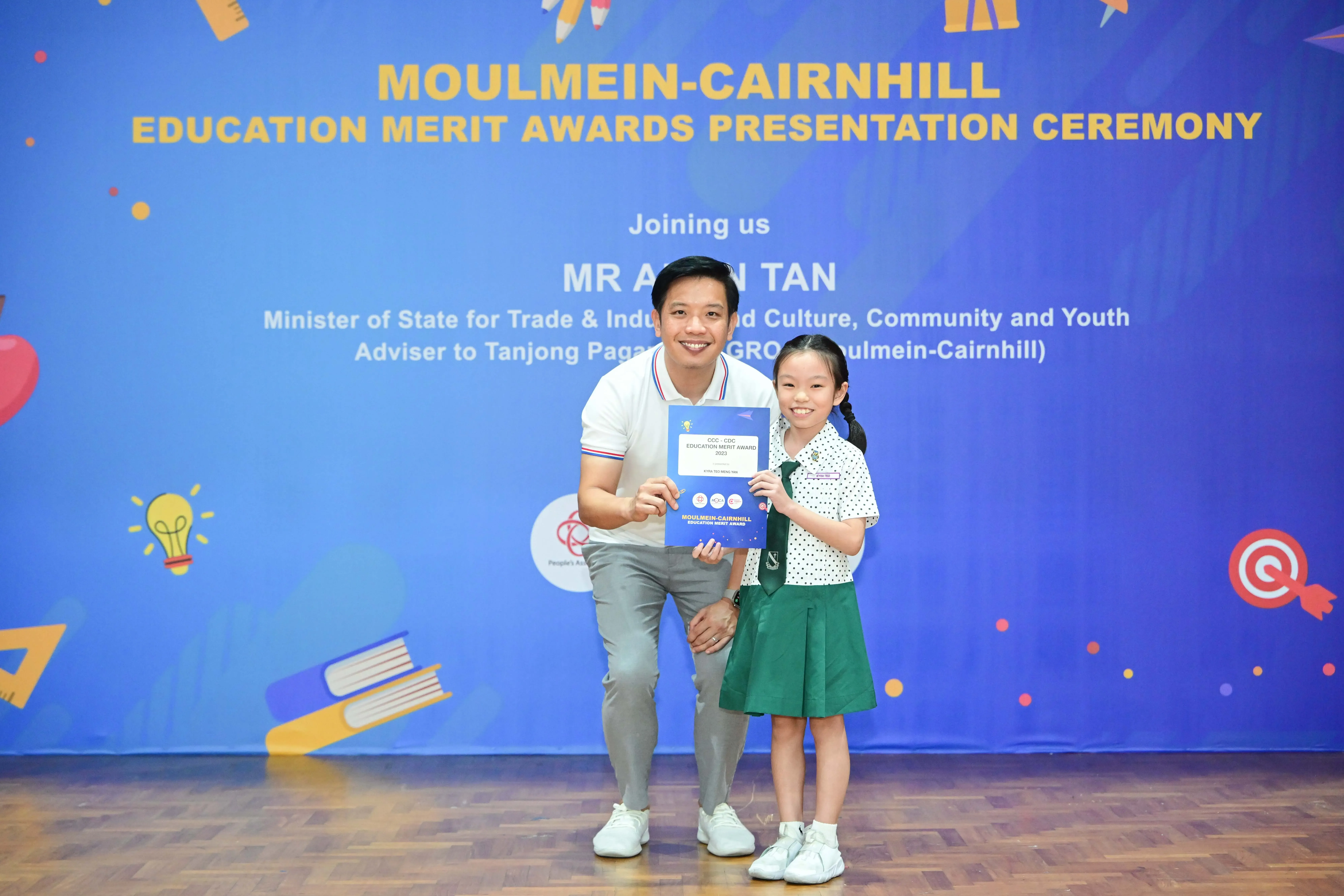A man and a young girl in school uniform hold a certificate at the Moulmein-Cairnhill Education Merit Awards ceremony.
