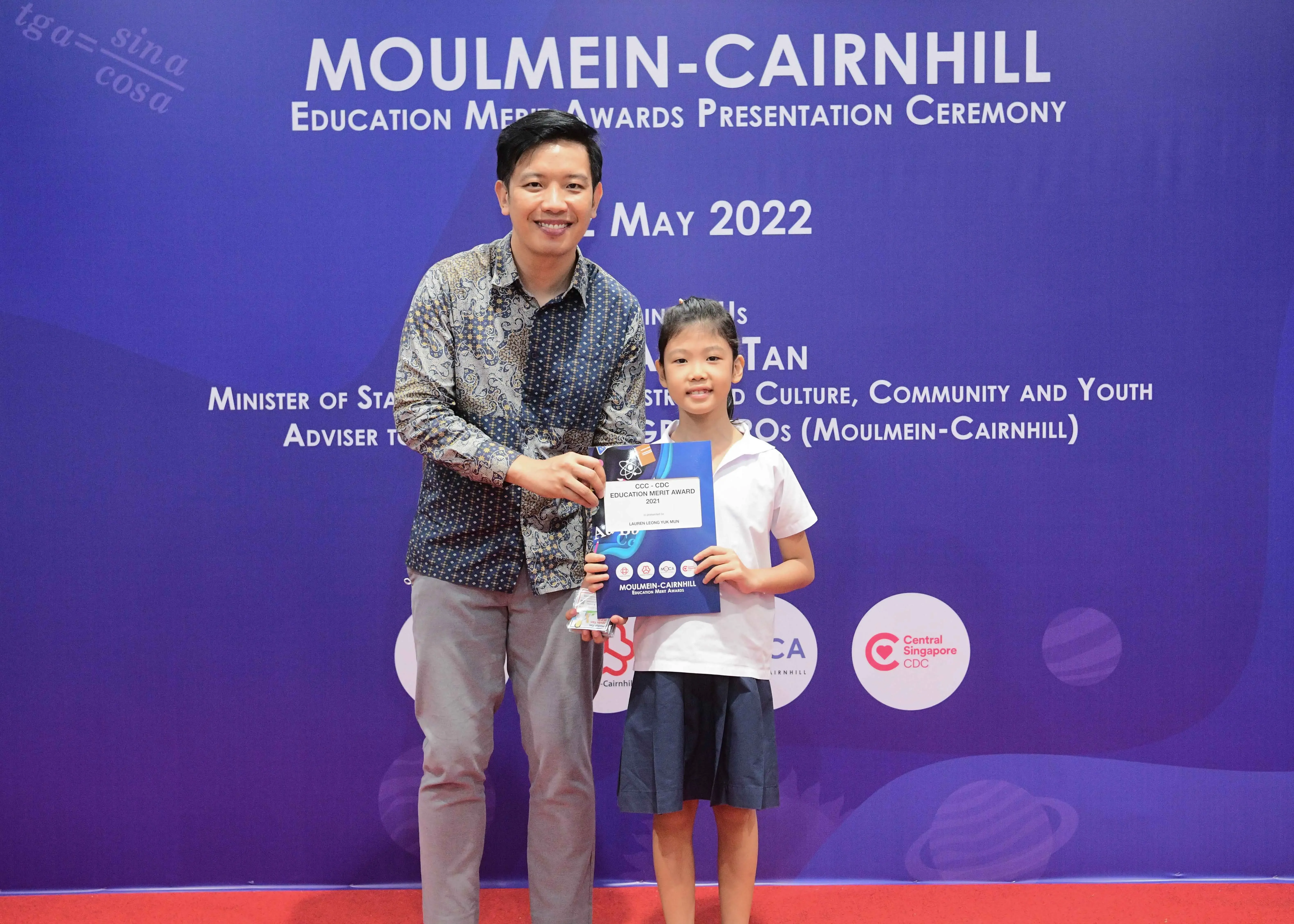 An adult and a young girl hold an award certificate at the Moulmein-Cairnhill Education Merit Awards Ceremony, May 2022.