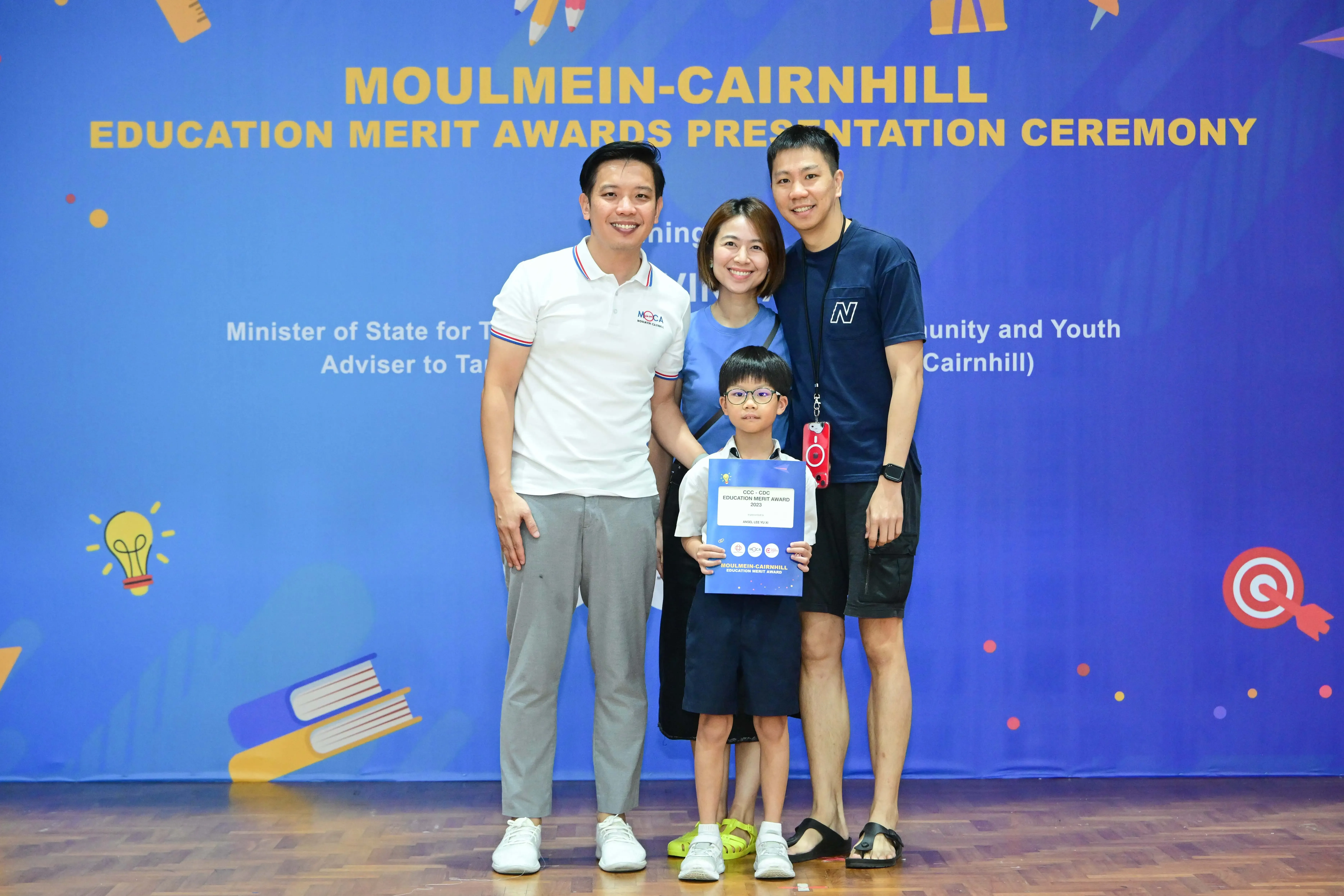 Three adults and a young boy holding an award certificate pose at the Moulmein-Cairnhill Education Merit Awards ceremony.