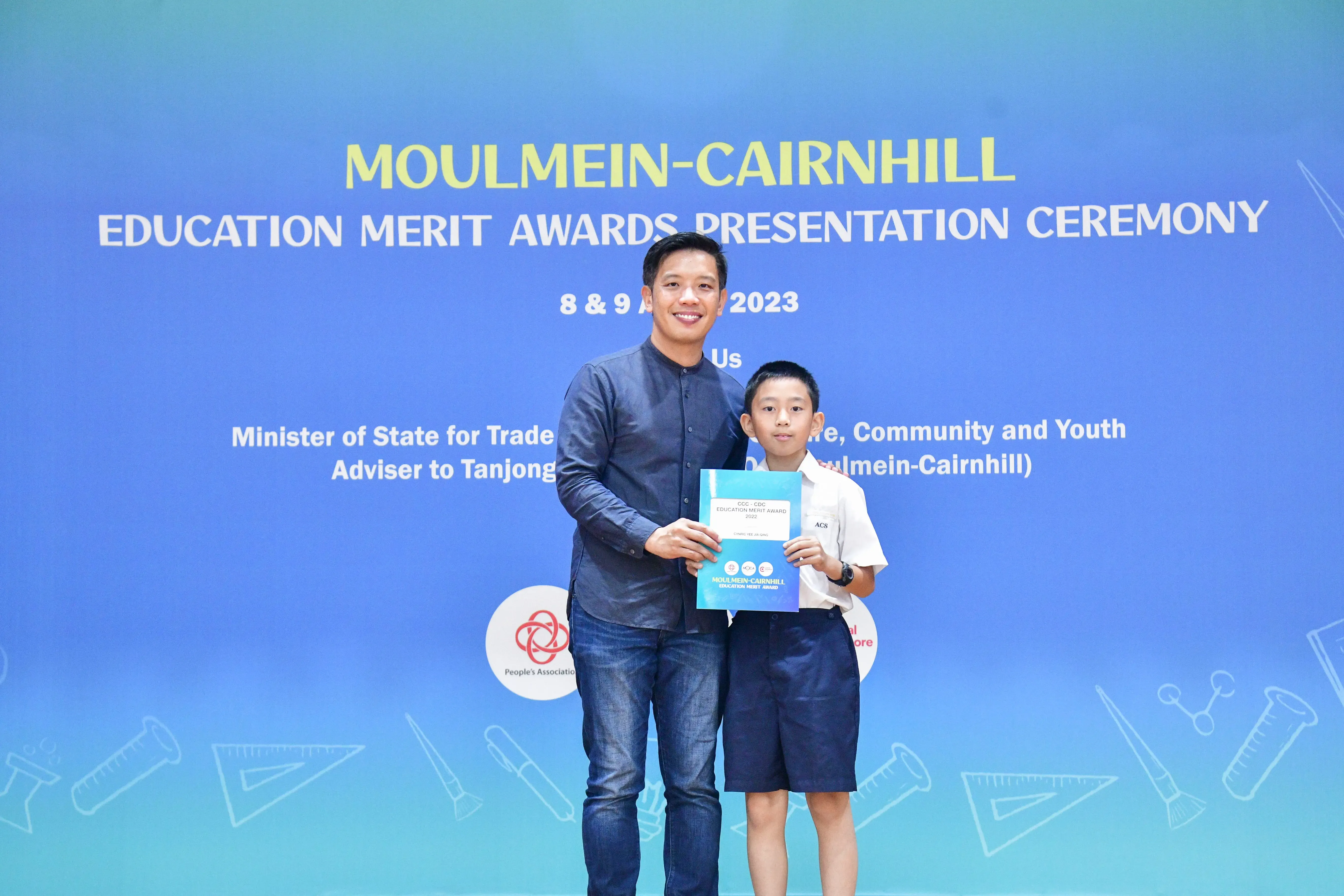 A man and a young boy hold a certificate at the Moulmein-Cairnhill Education Merit Awards Ceremony 2023.