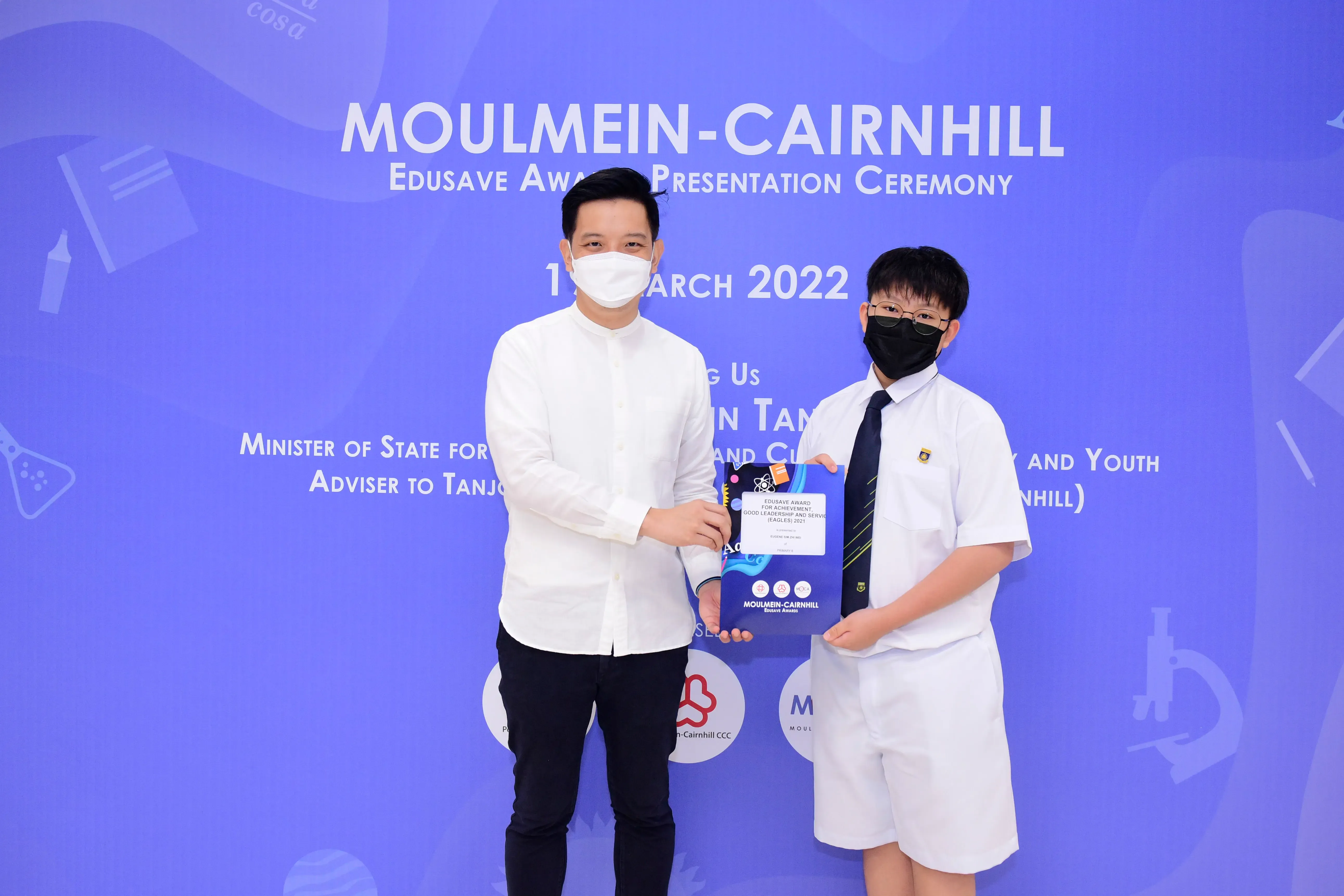 Two masked individuals hold a certificate at the Moulmein-Cairnhill Edusave Award Presentation Ceremony, March 2022.