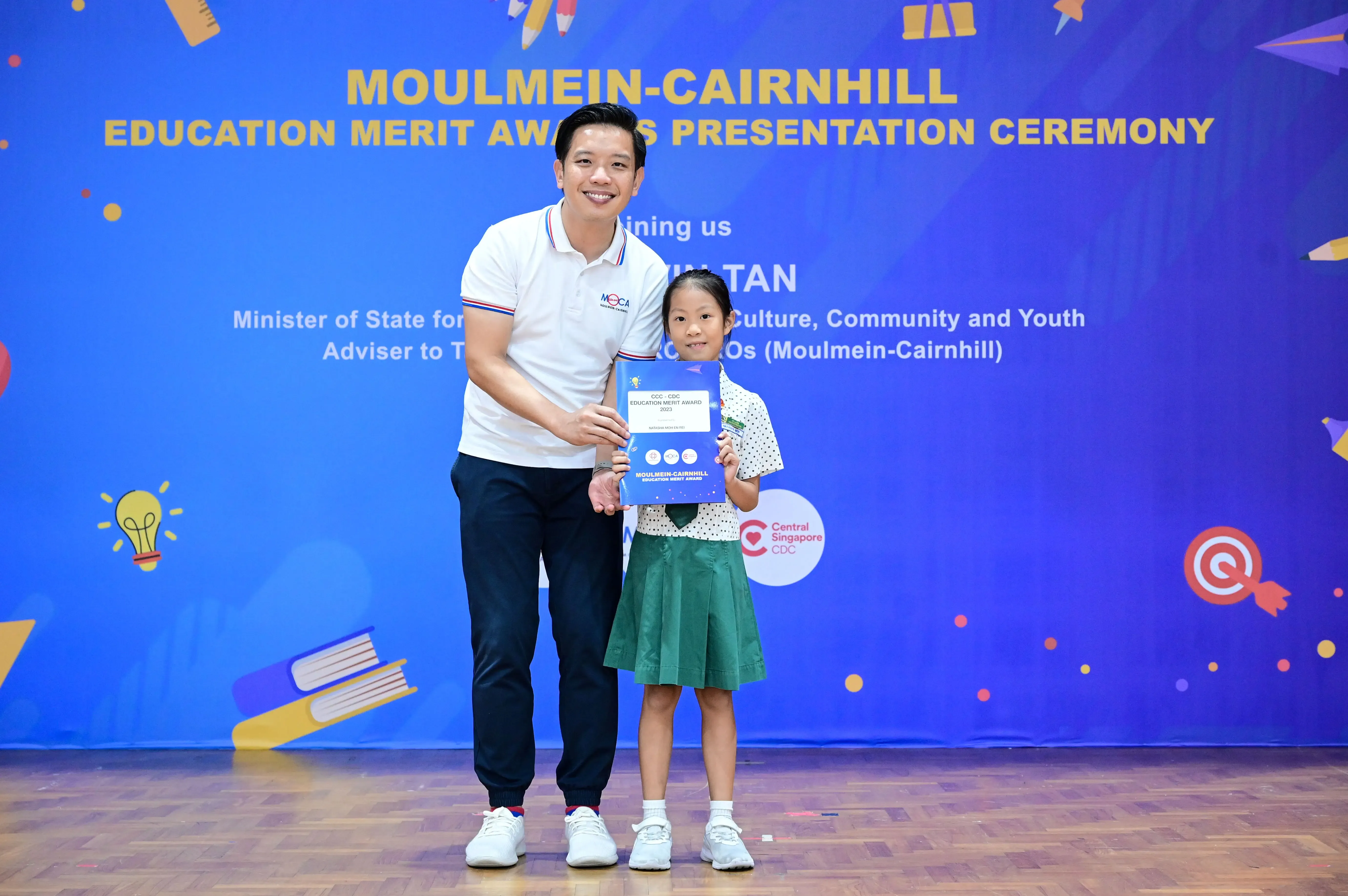 A man and a young girl hold a certificate at the Moulmein-Cairnhill Education Merit Awards Presentation Ceremony.