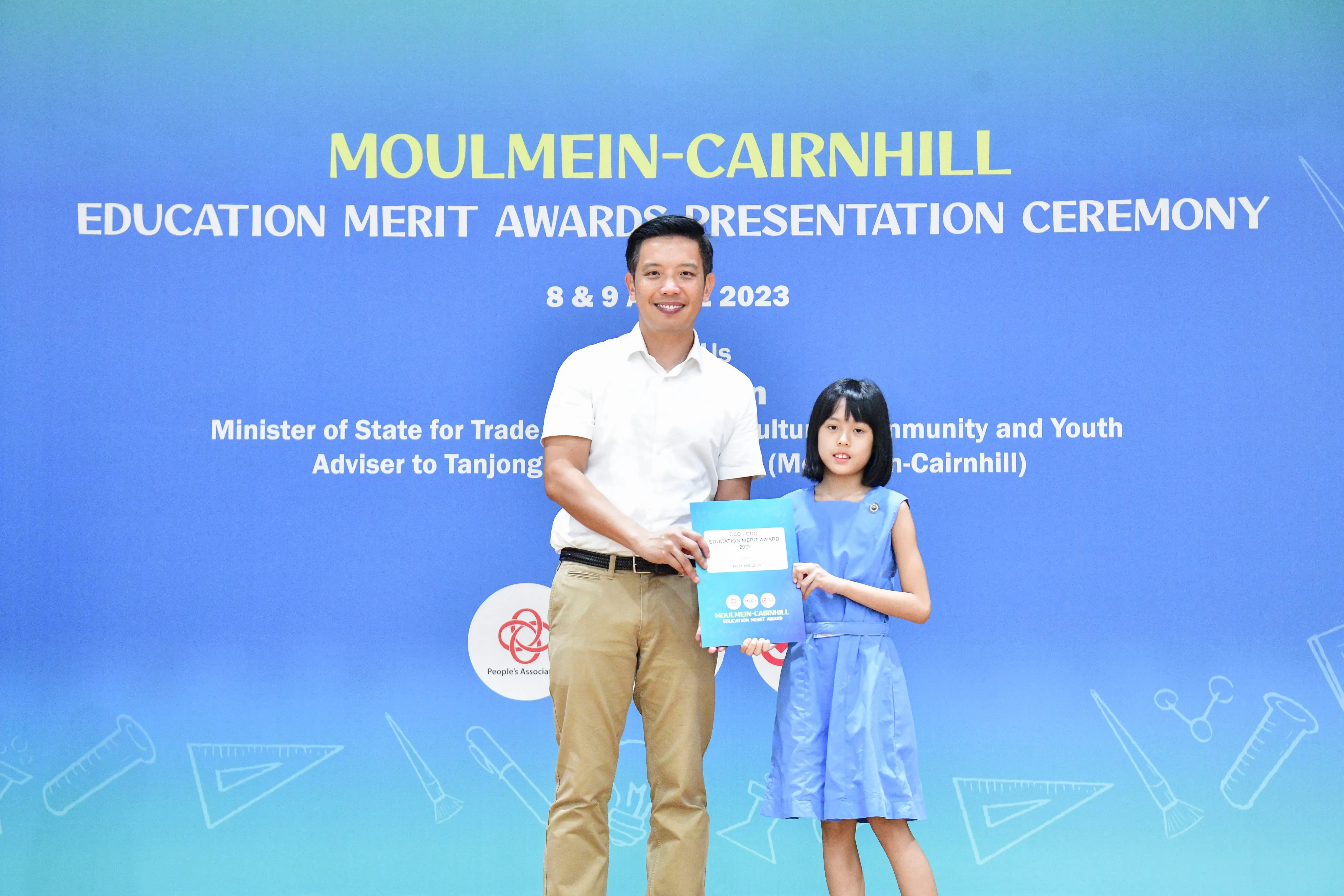 A man and a young girl hold a certificate together at the Moulmein-Cairnhill Education Merit Awards Ceremony 2023.
