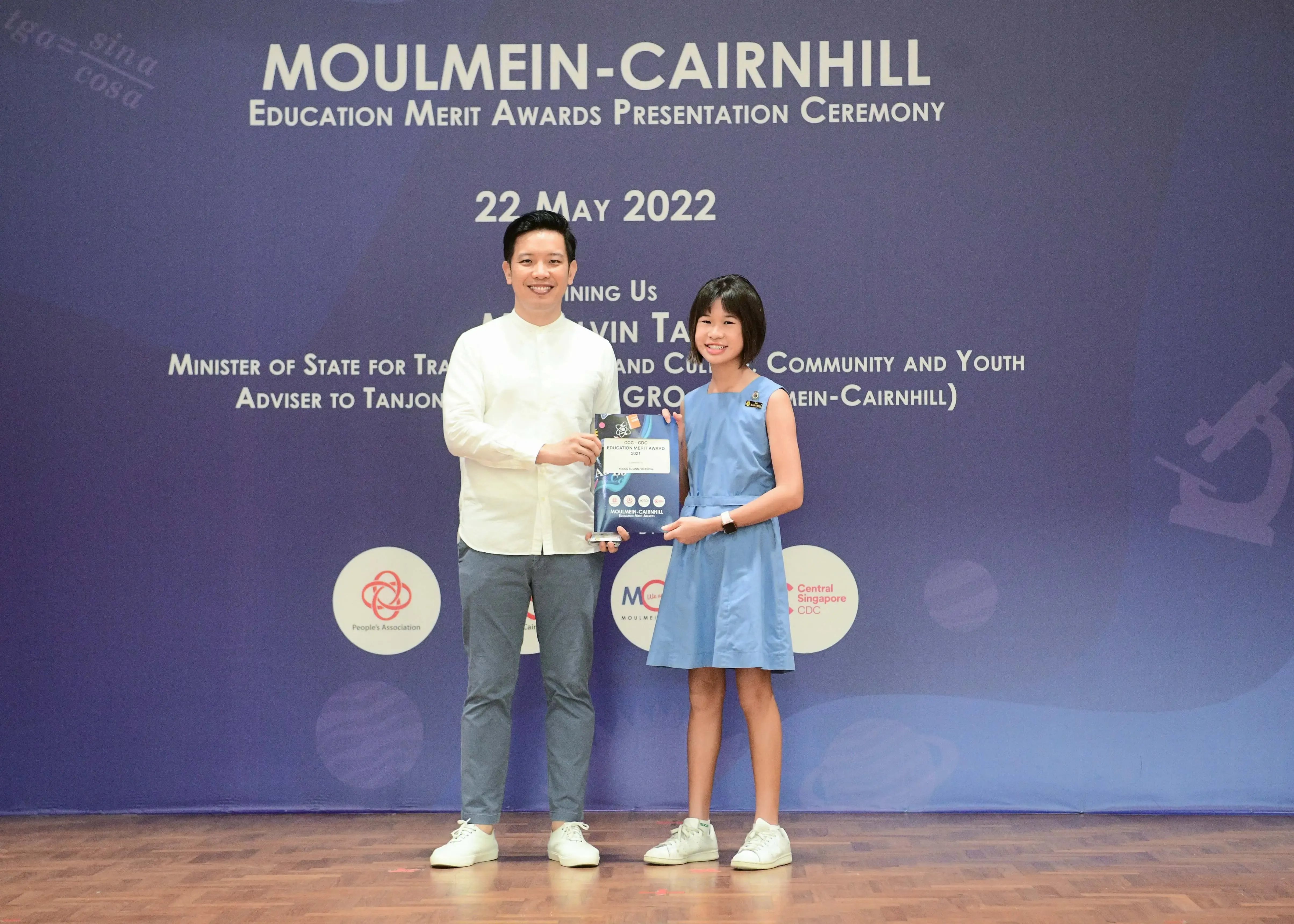 Two people smile and hold an award plaque at the Moulmein-Cairnhill Education Merit Awards Ceremony on 22 May 2022.