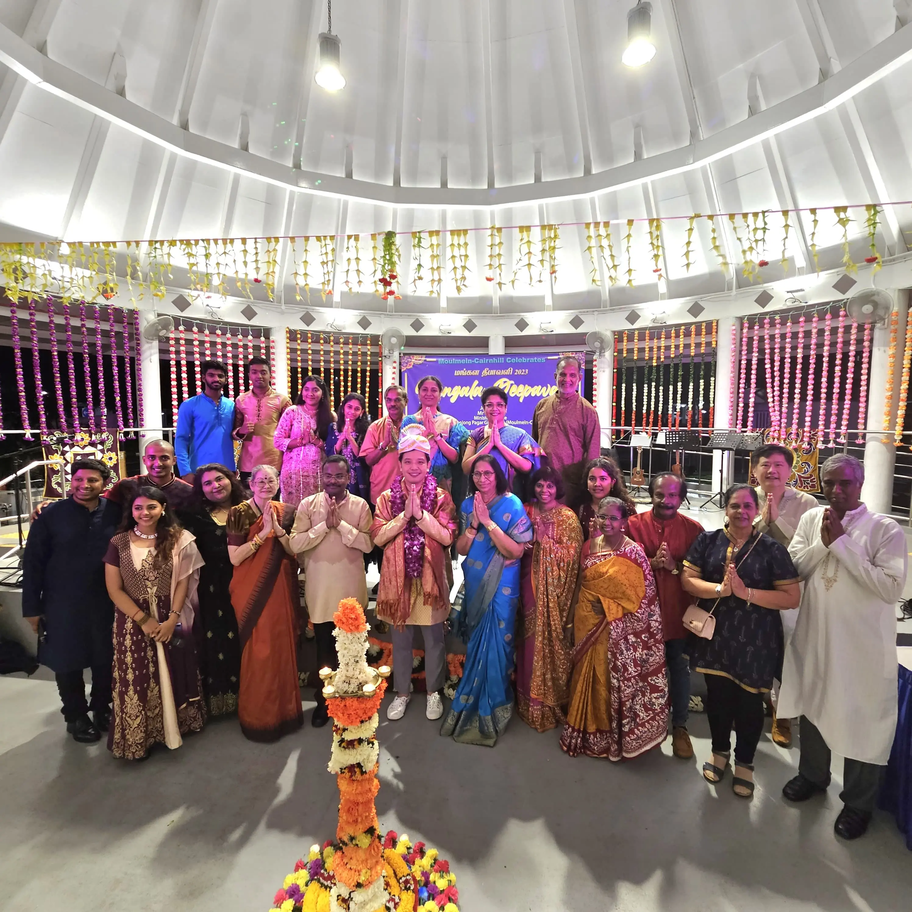 Group of people in traditional Indian attire posing at a Diwali celebration with colorful flower decorations.