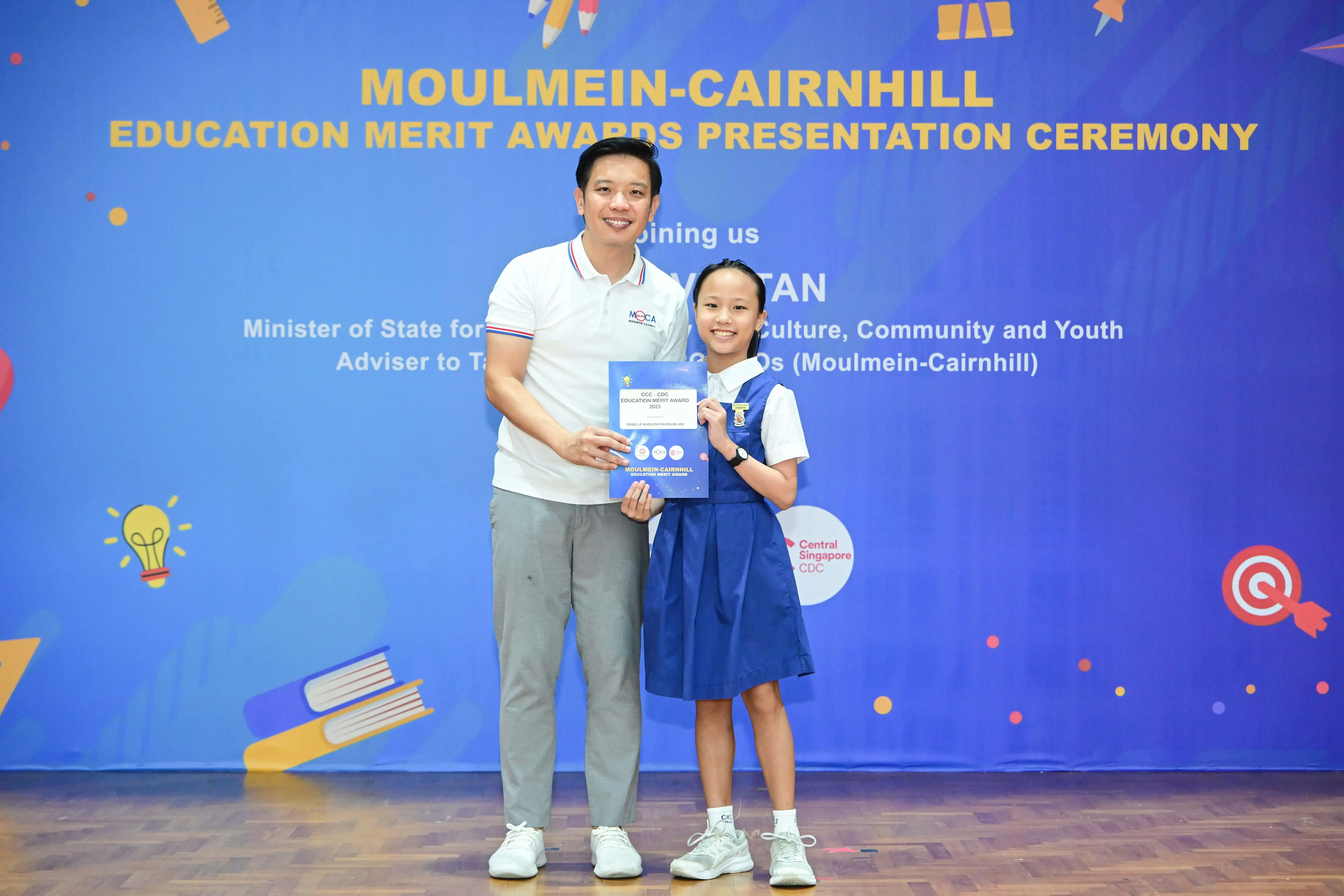 A man and a young girl in school uniform hold a certificate at the Moulmein-Cairnhill Education Merit Awards ceremony.