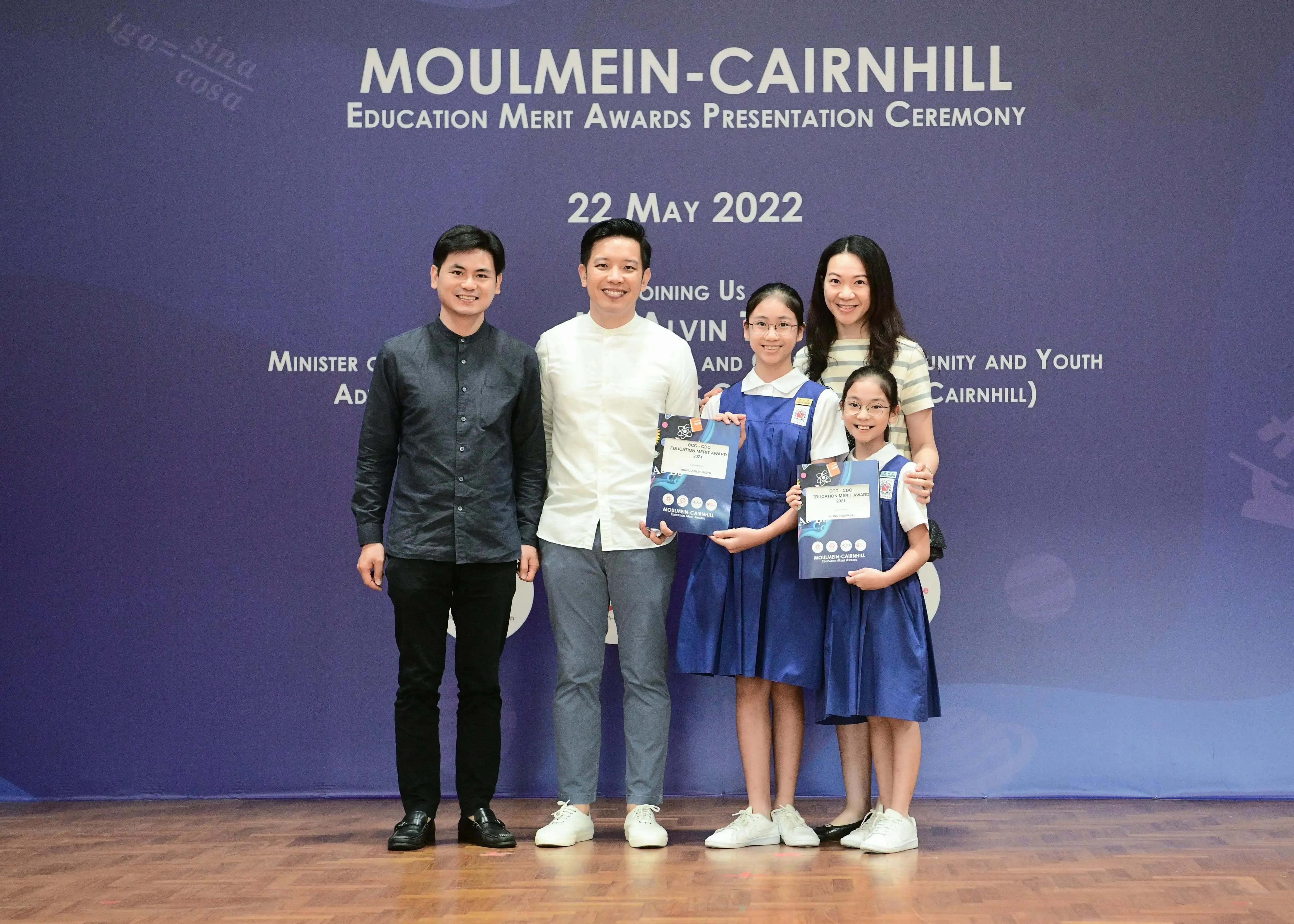 Five people pose at the Moulmein-Cairnhill Education Merit Awards Ceremony on 22 May 2022, two girls holding award booklets.
