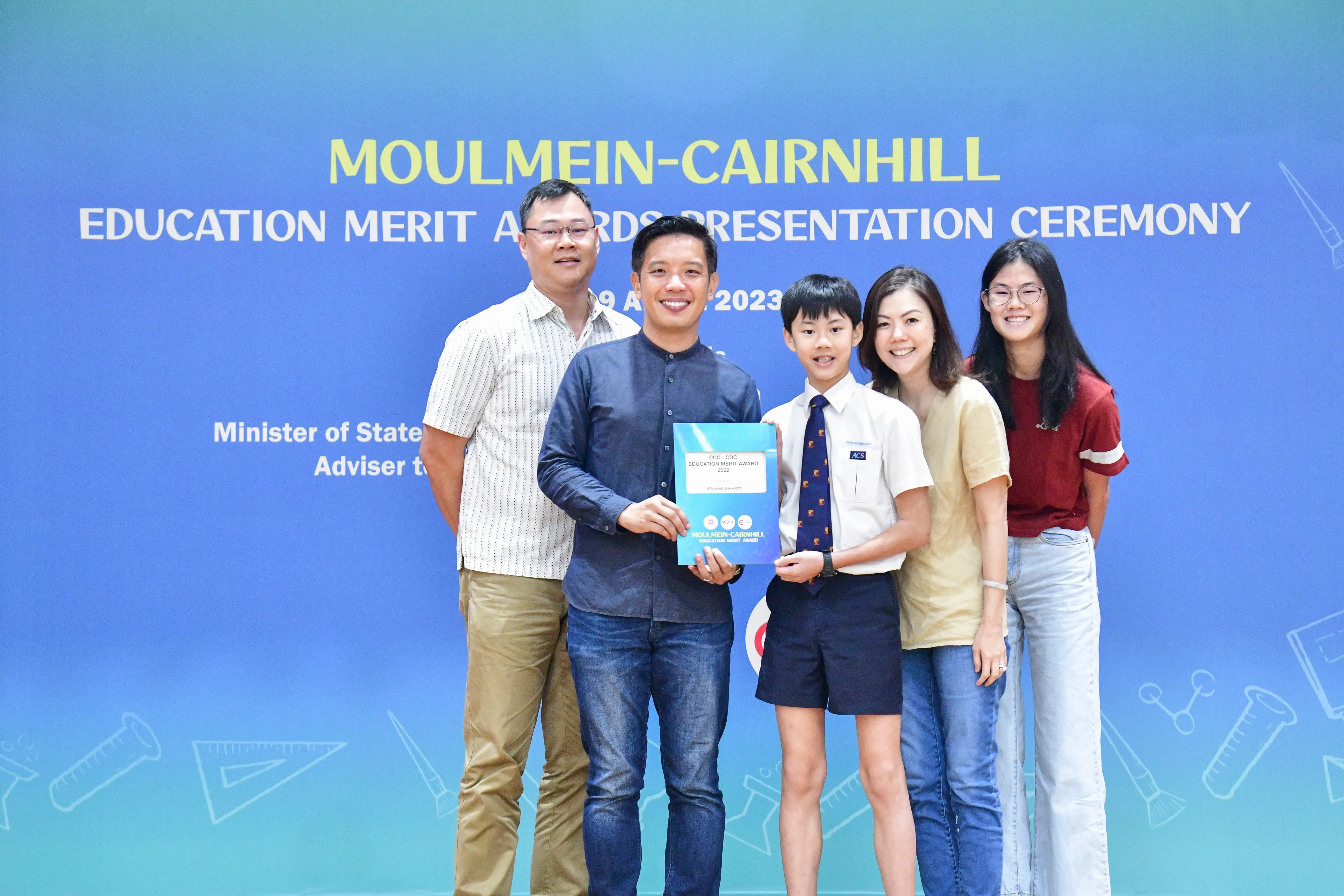 Five people pose at the Moulmein-Cairnhill Education Merit Awards Presentation Ceremony 2023, with a boy holding a certificate.