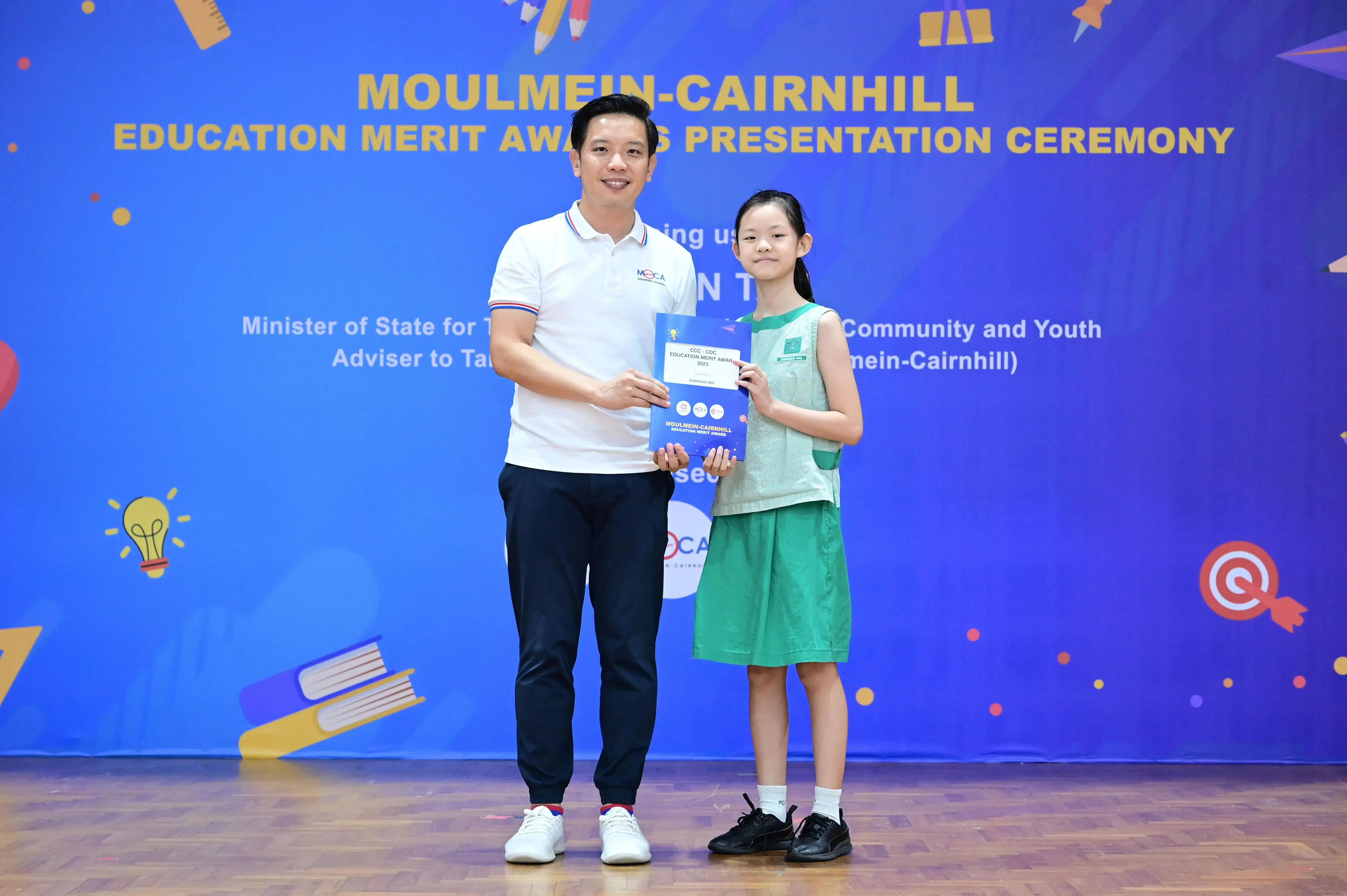 A man and a young girl hold an award certificate at the Moulmein-Cairnhill Education Merit Awards Presentation Ceremony.