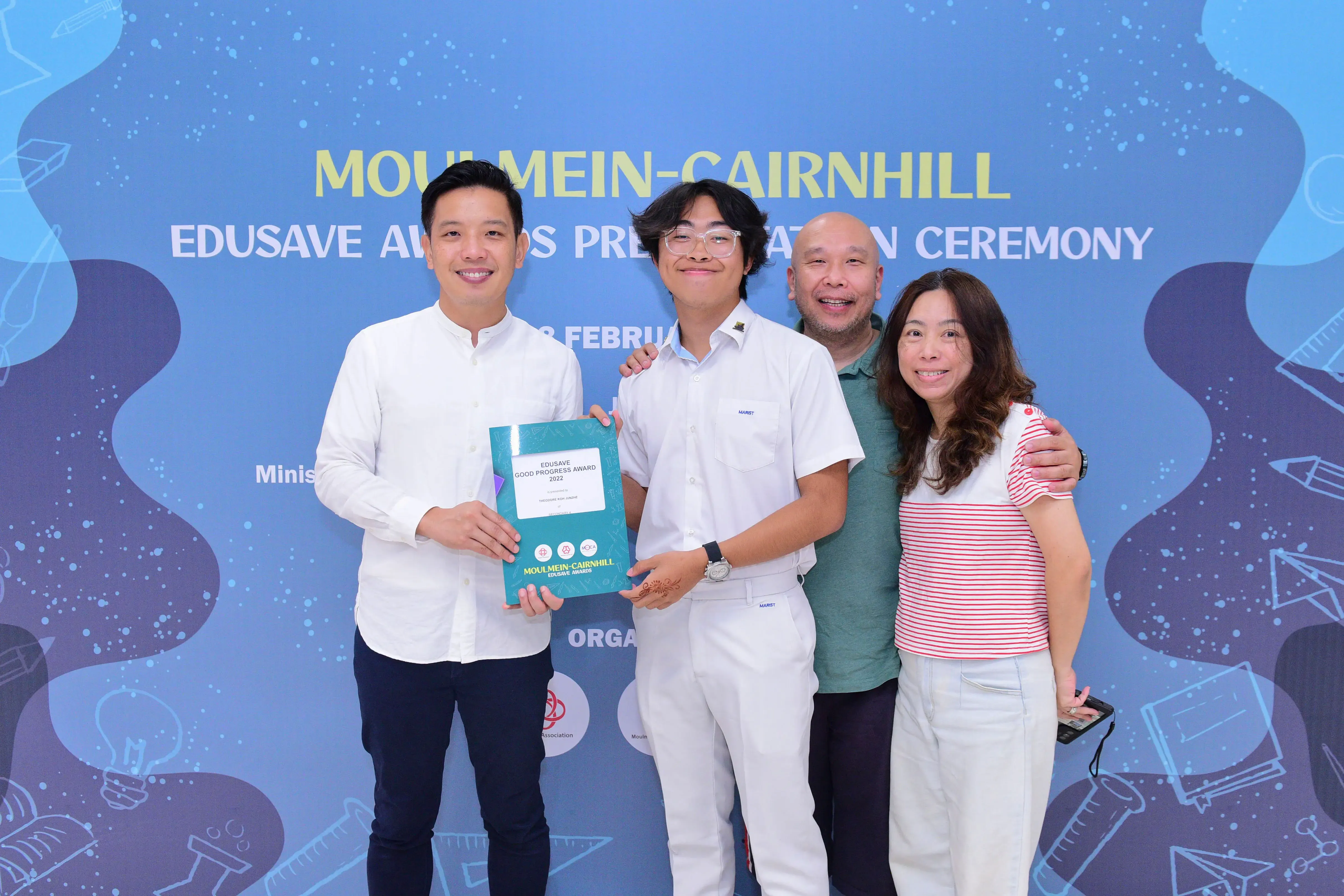 Four smiling people pose at the Moulmein-Cairnhill Edusave Awards Presentation Ceremony, holding an award certificate.