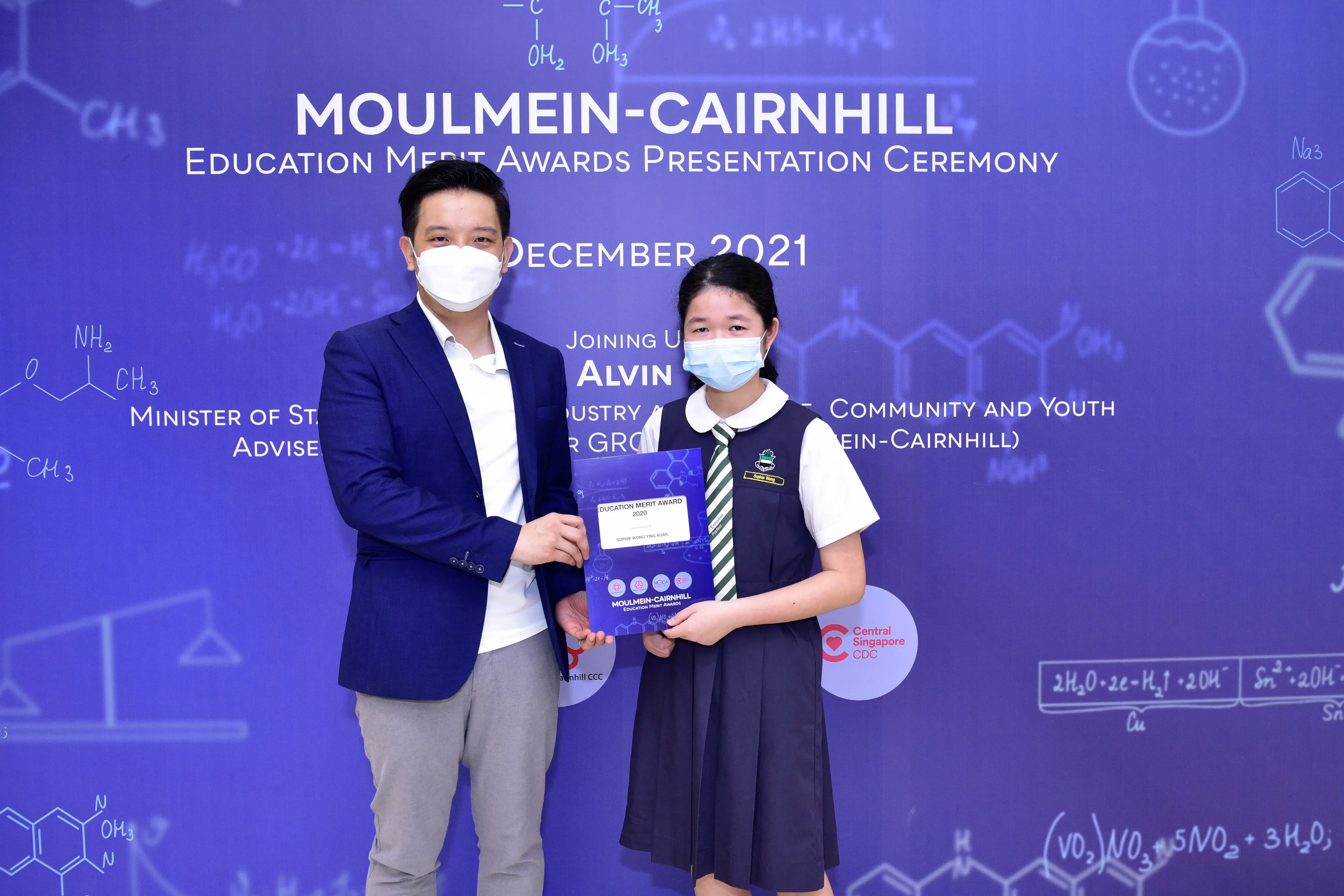 A man and a young girl in school uniform hold an award certificate at the Moulmein-Cairnhill Education Merit Awards 2021.