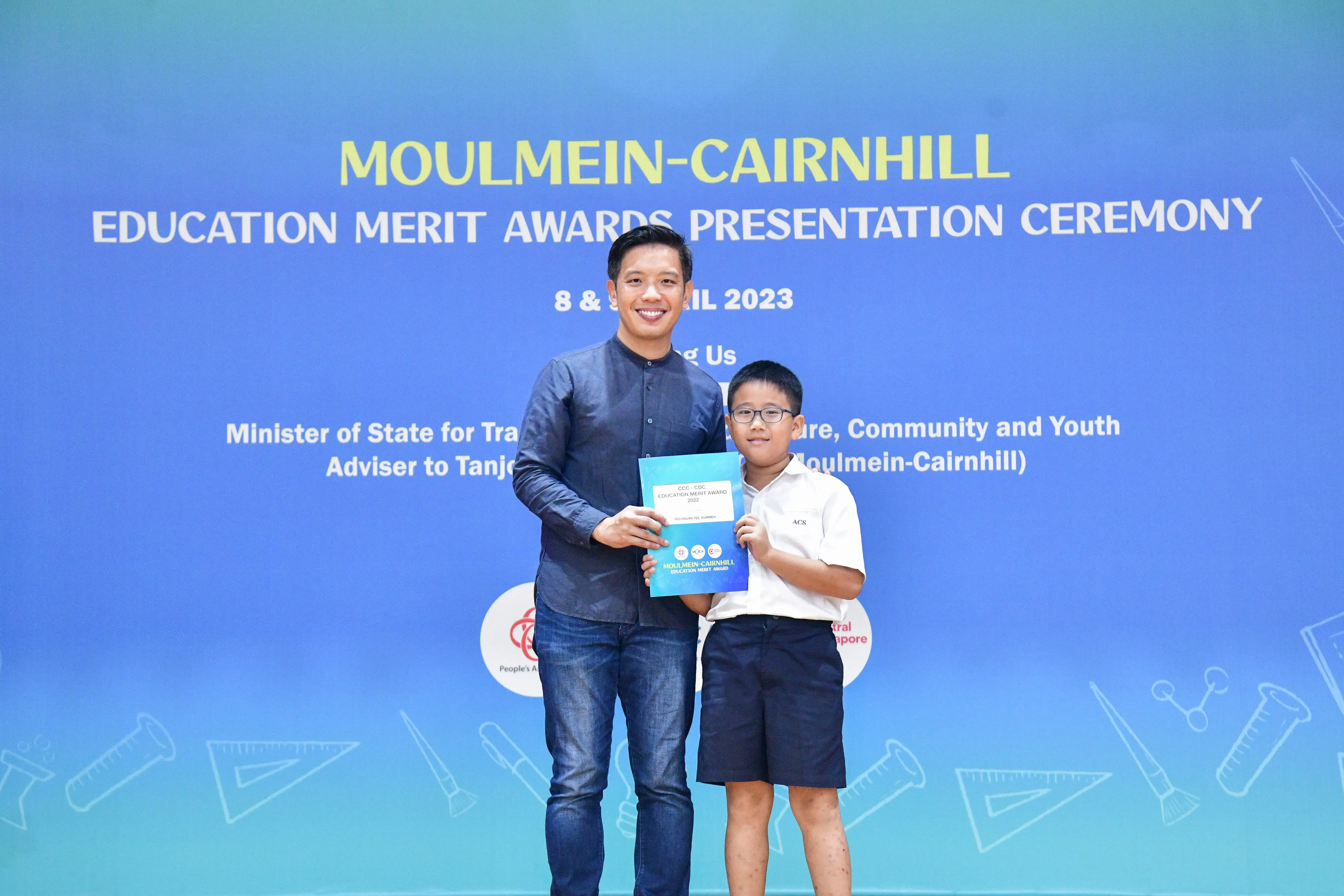 An adult man and a young boy hold a certificate together at the Moulmein-Cairnhill Education Merit Awards Ceremony 2023.
