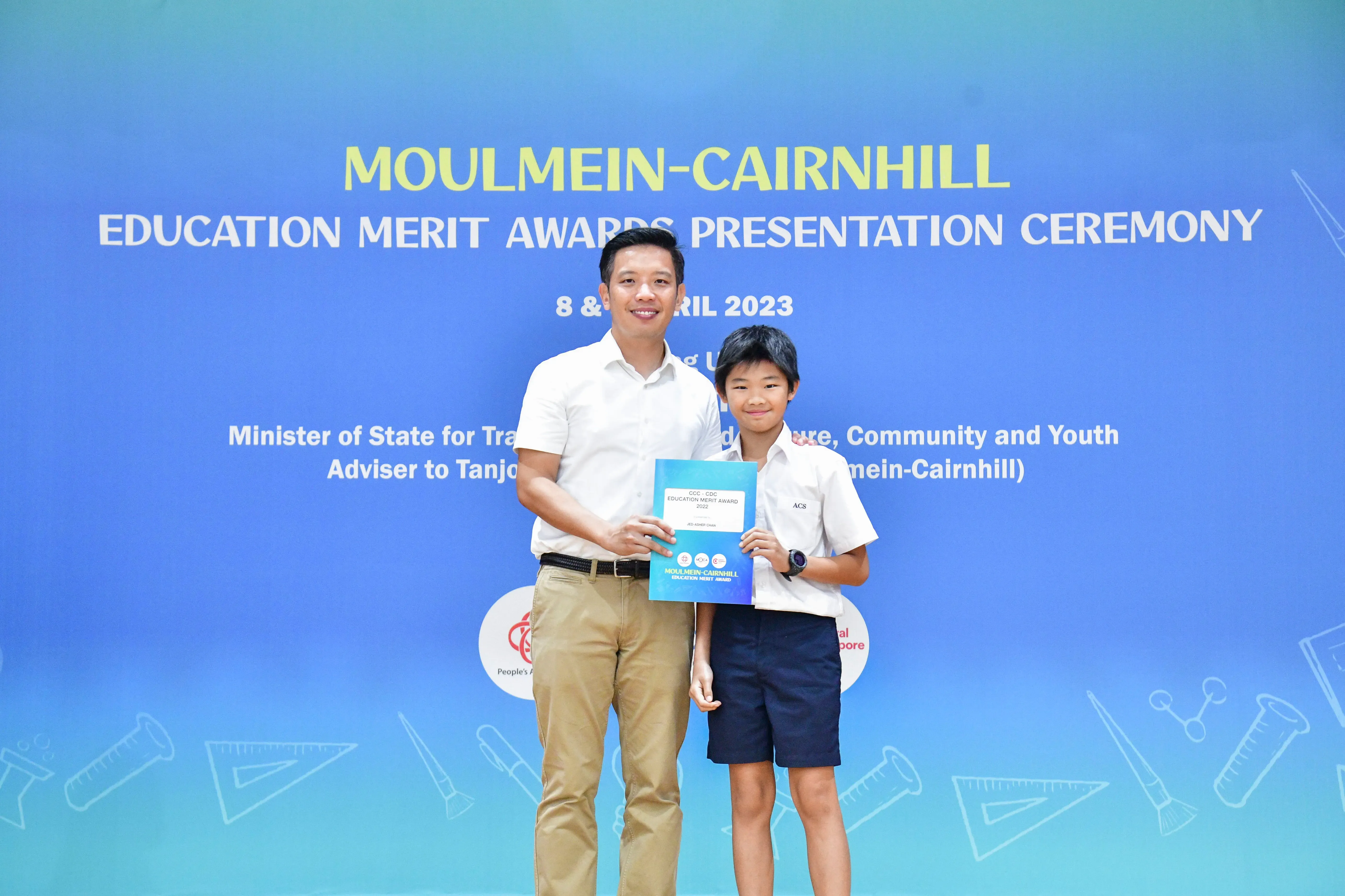 A man and a young boy hold a certificate together at the Moulmein-Cairnhill Education Merit Awards Ceremony, April 2023.