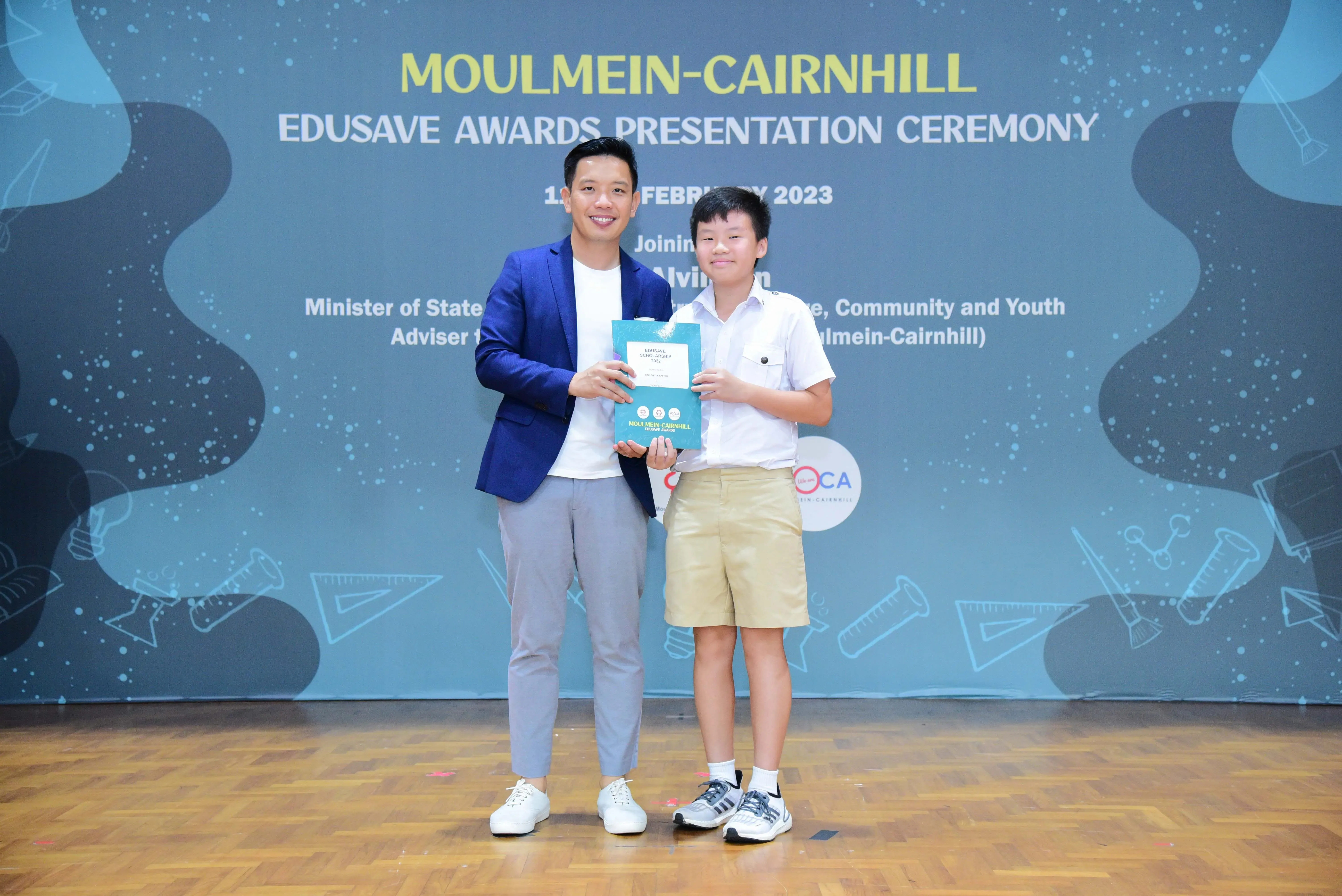 Man in blue blazer and young boy in school uniform hold an award at Moulmein-Cairnhill Edusave Awards Ceremony 2023.