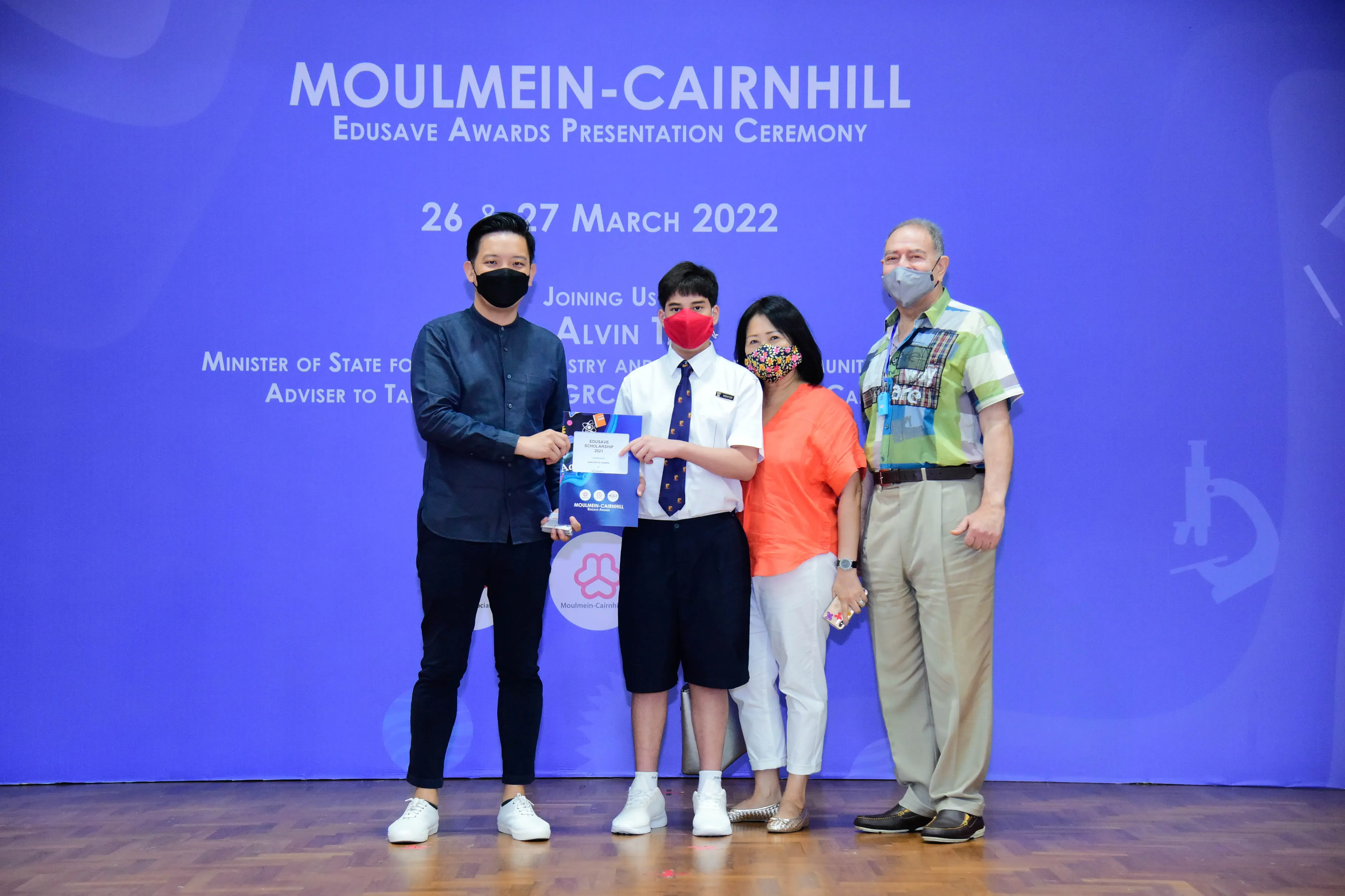 Four masked people pose on stage at the Moulmein-Cairnhill Edusave Awards Presentation Ceremony, March 2022.
